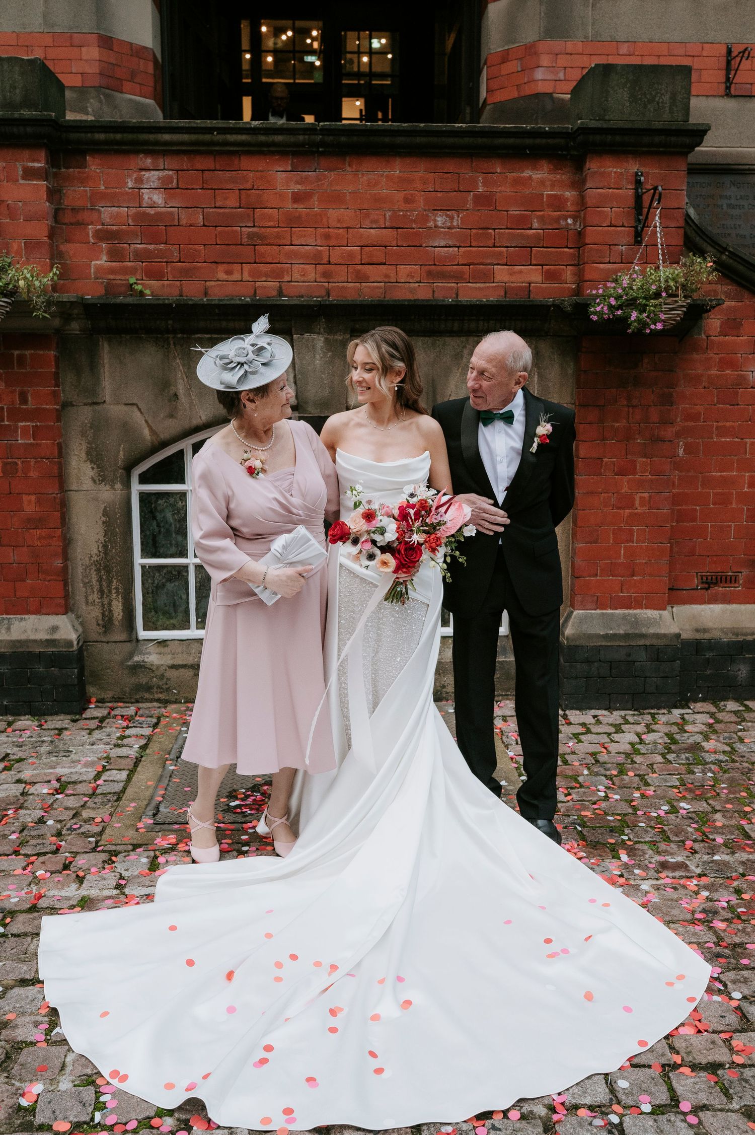 White wedding dress train spreads elegantly across cobblestone path with scattered rose petals.
