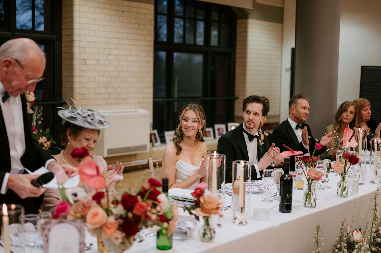 Wedding reception dinner party with guests seated at a decorated table with floral centerpieces and candlelight.
