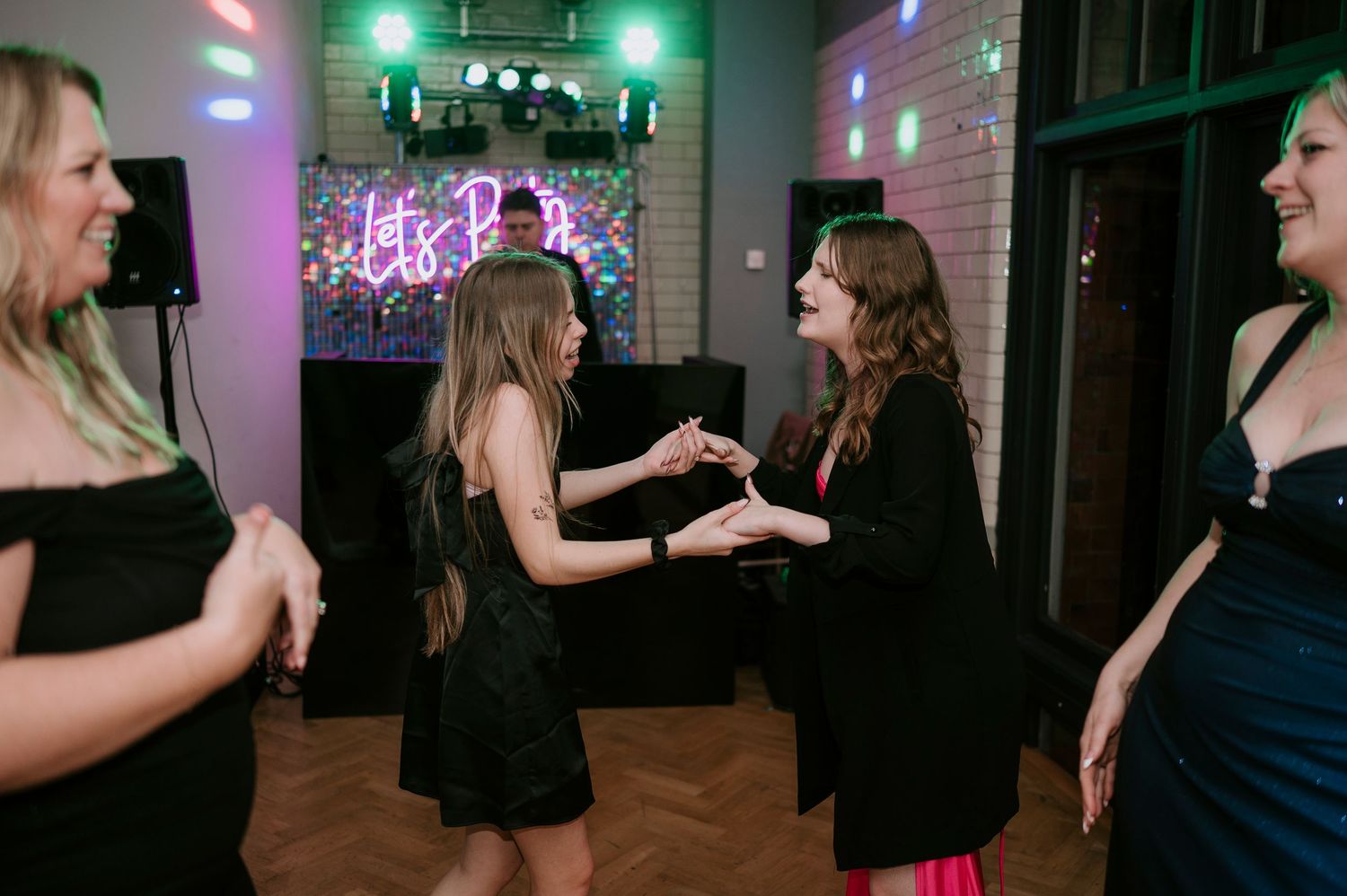A group of guests dance together on a dark dance floor illuminated by colorful party lights.
