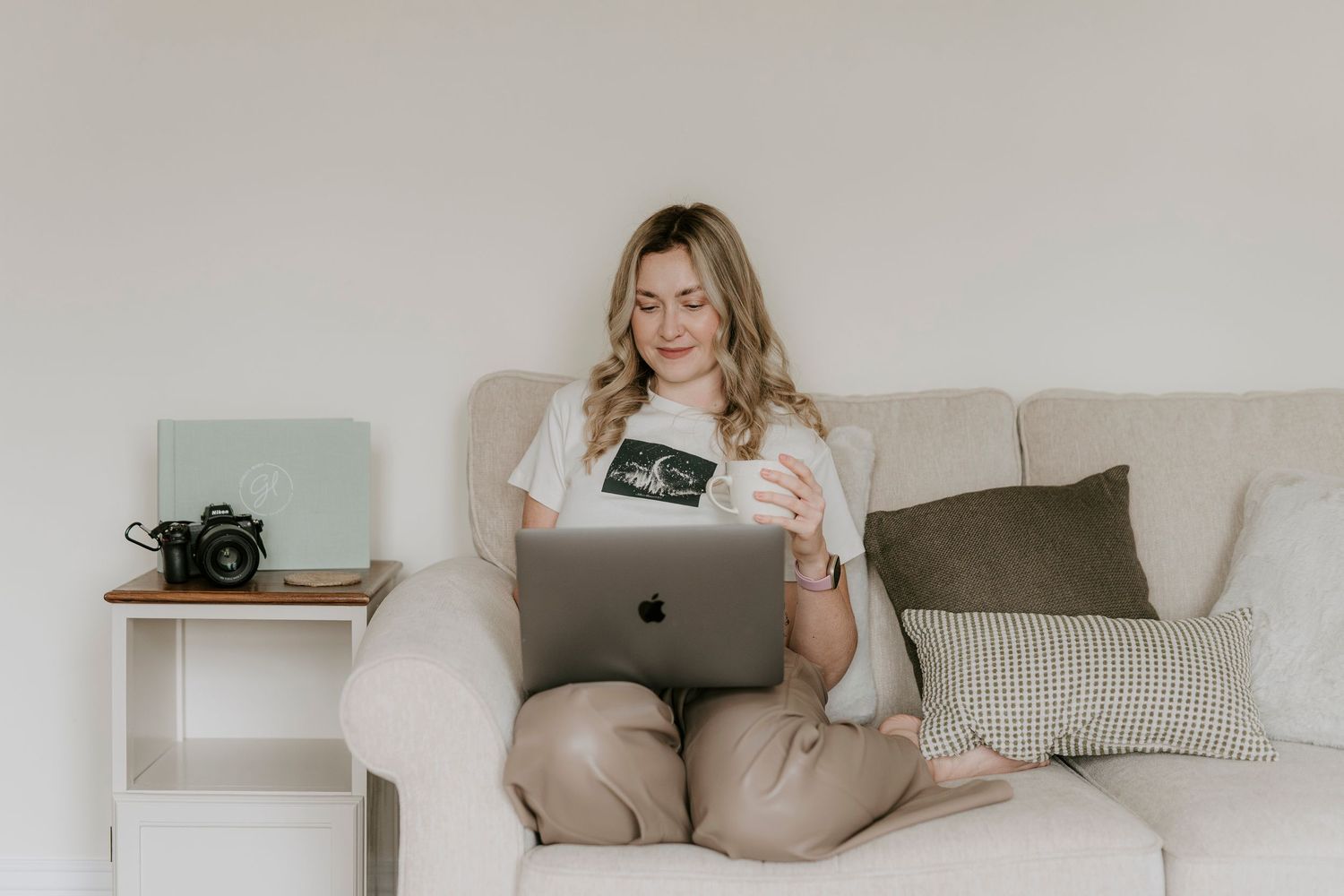 Woman in cozy beige loungewear relaxes on white sofa while reading and enjoying quiet time at home.
