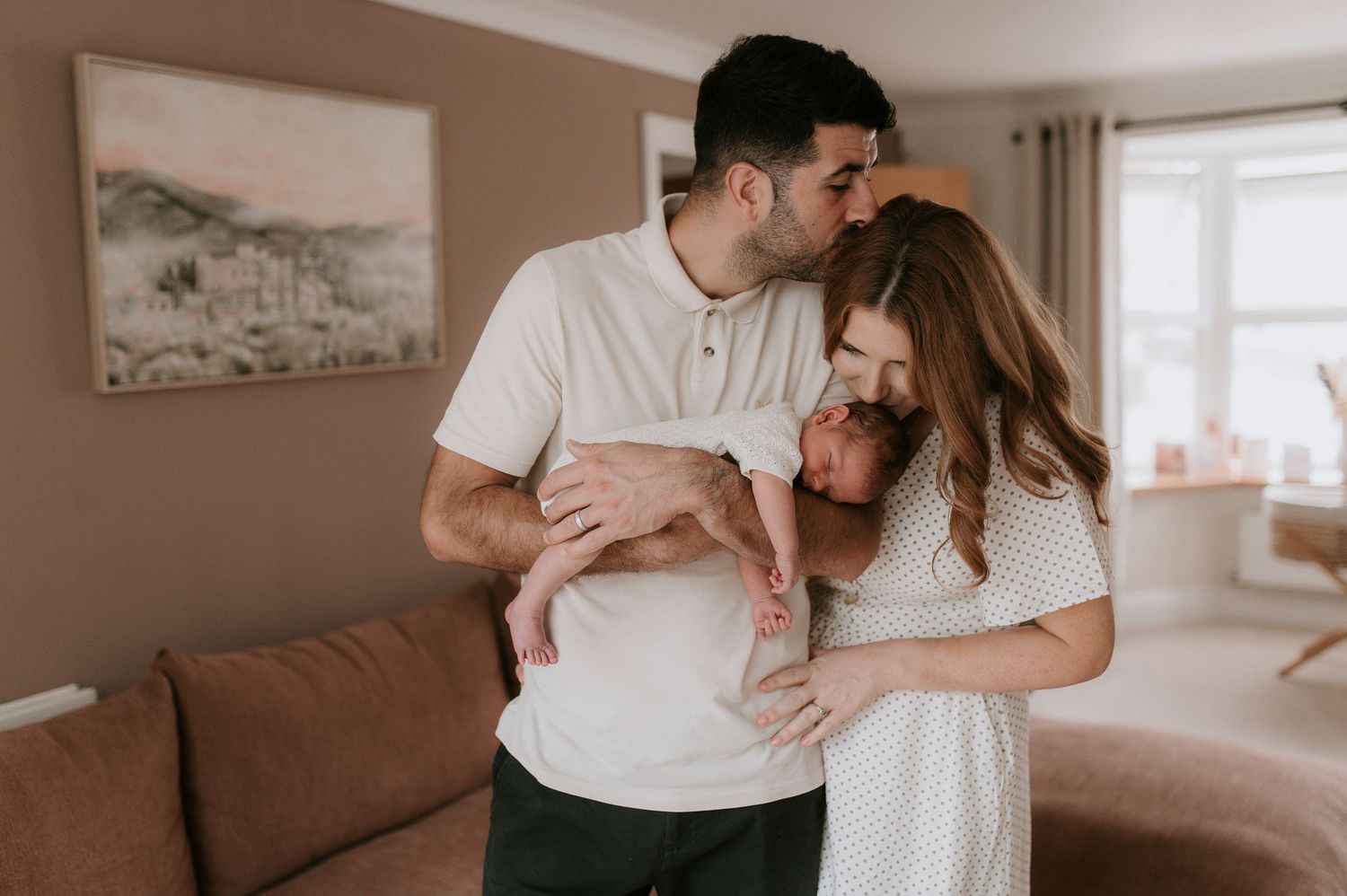 A romantic couple in white clothing embraces tenderly in a sunlit living room.