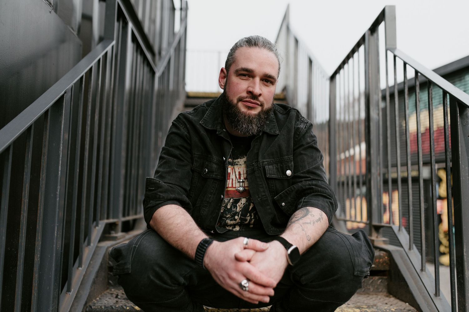 A person in black clothing sits on urban metal stairs while smiling at the camera.