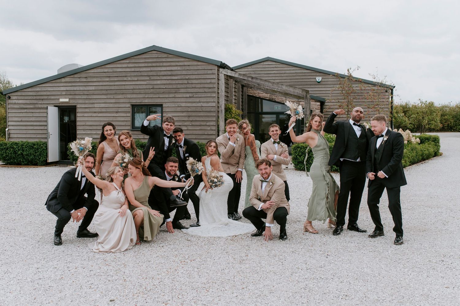 Wedding party poses together in a creative panoramic sequence outside a gray building on a cloudy day.