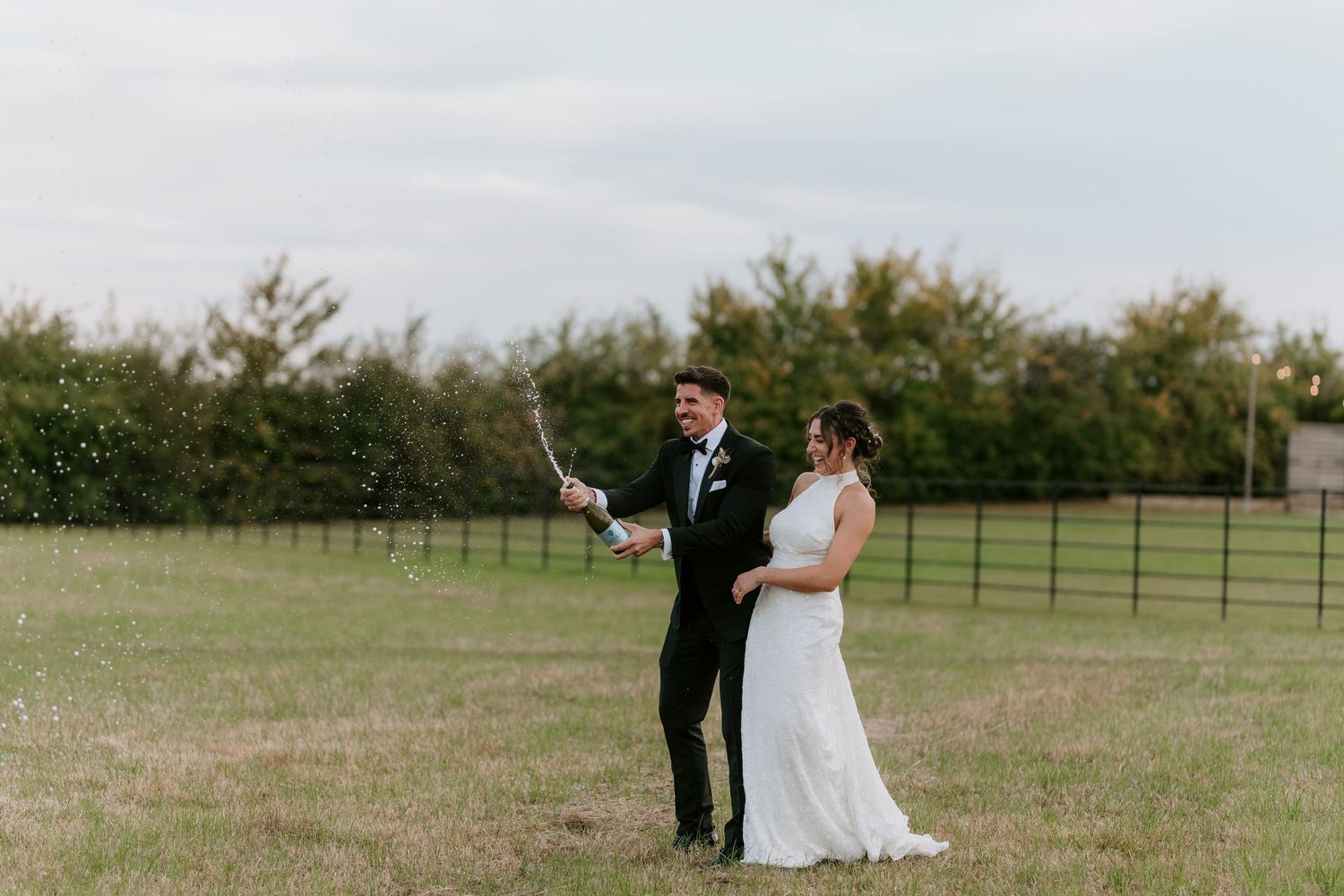 Newlywed couple walks hand in hand through a serene meadow during their outdoor wedding photo session.