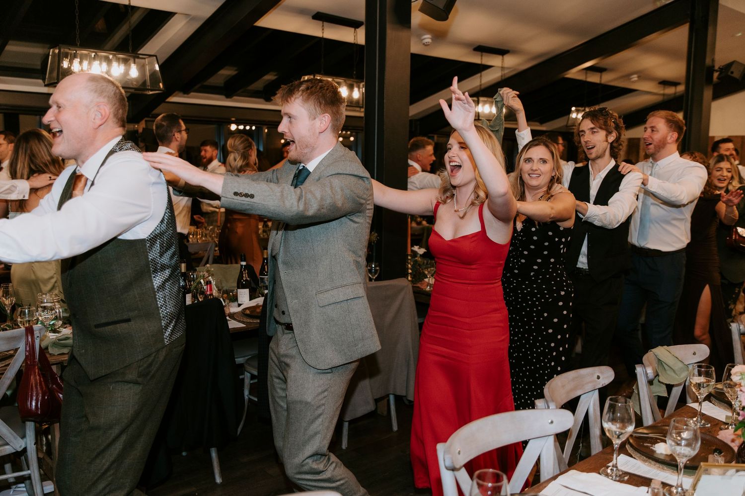 Wedding guests dance in celebration at a reception, with a woman in red dress and others in formal attire enjoying the moment.