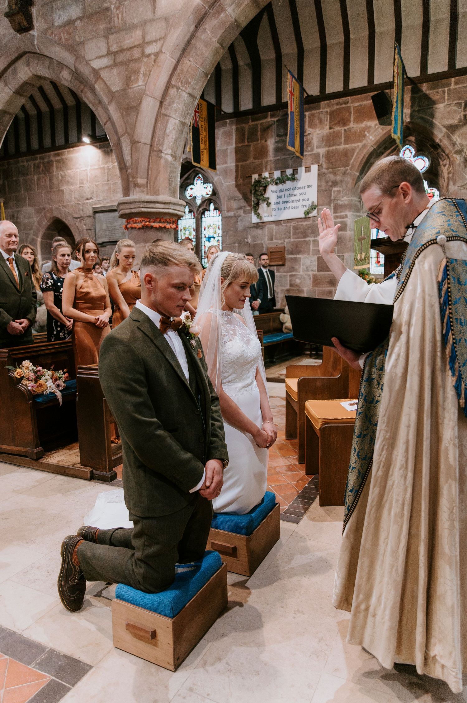 A traditional church wedding ceremony takes place inside a stone chapel with Gothic arches and wooden pews.