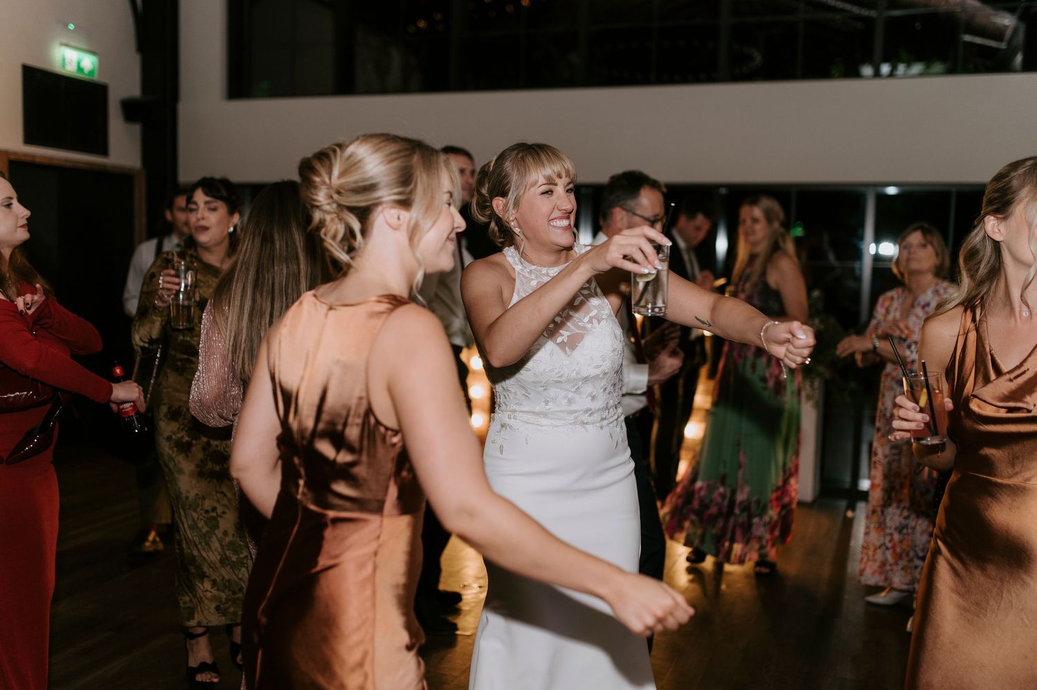 Wedding guests dance and celebrate on a dimly lit dance floor during a lively reception party.