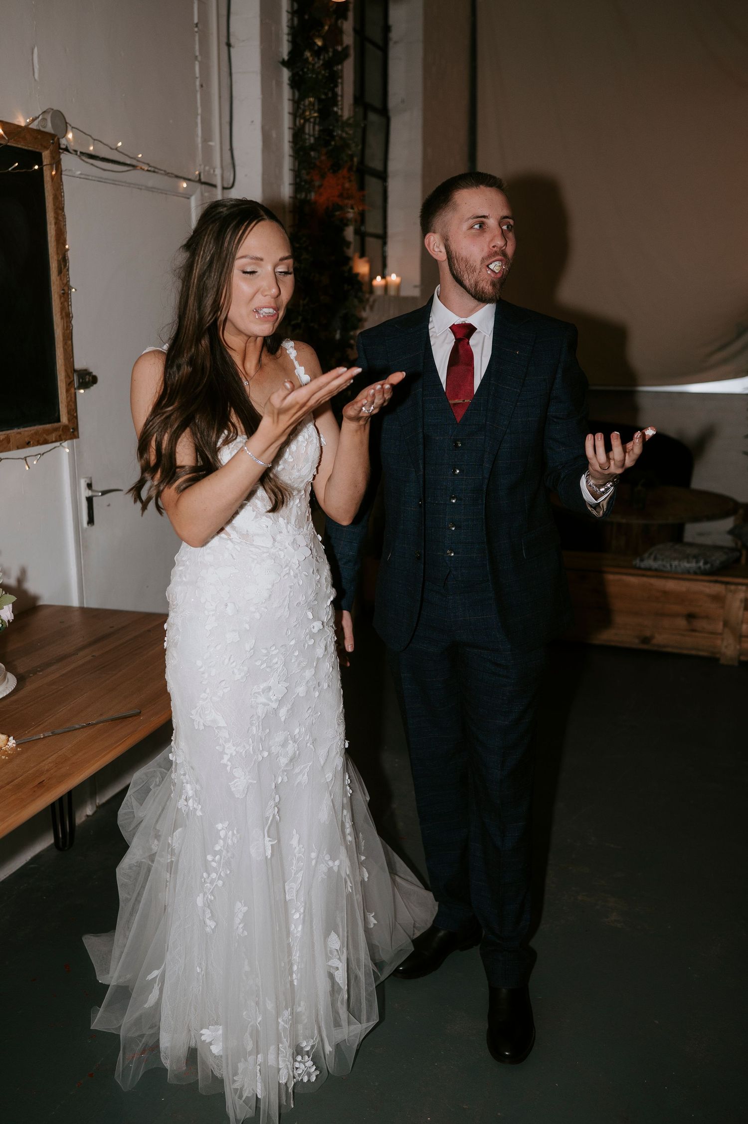 Bride and groom laughing and clapping hands together during wedding reception in rustic venue.