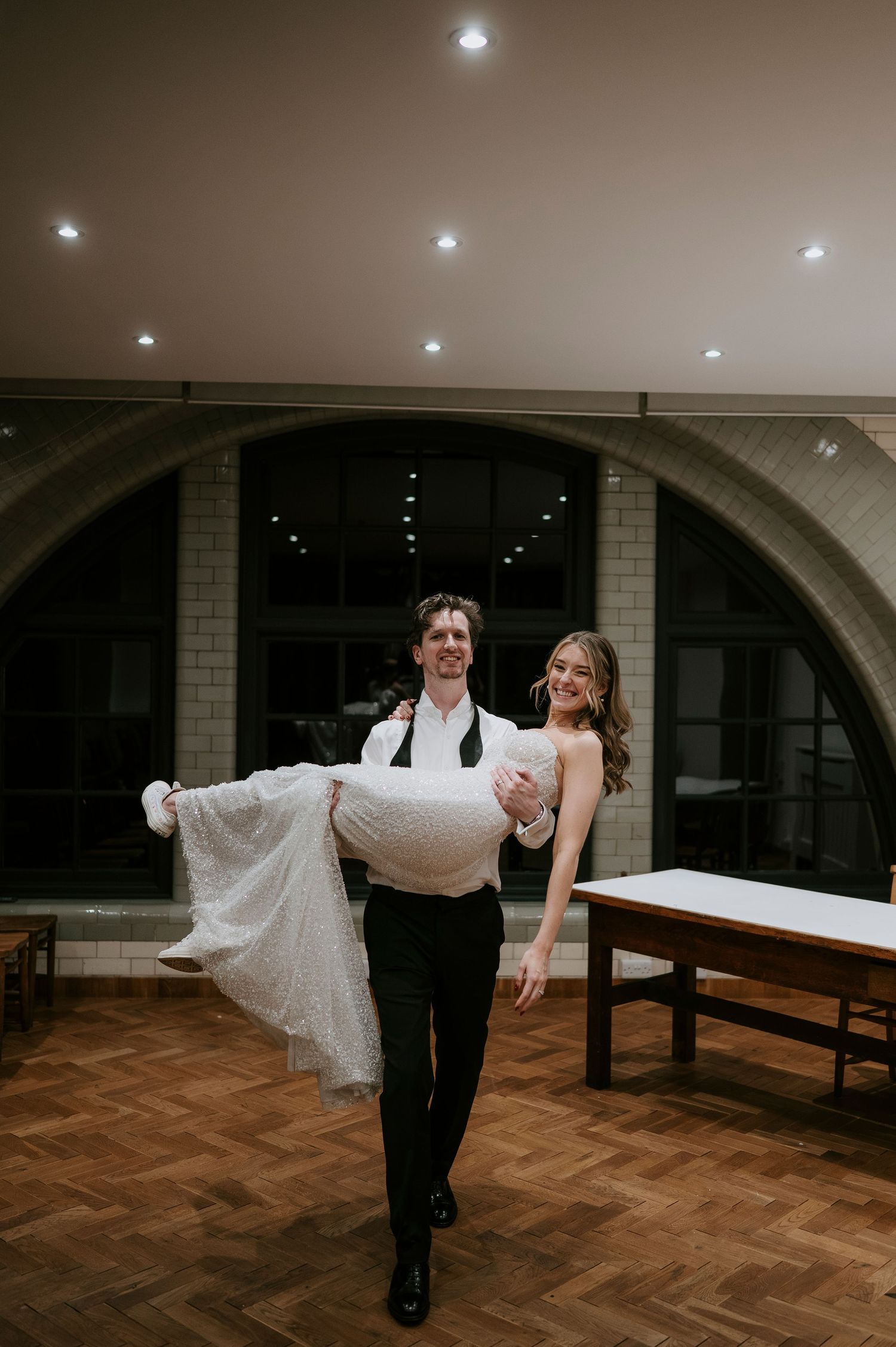 A couple performs a romantic dance lift sequence in an elegant indoor venue with arched ceilings and wooden floors.