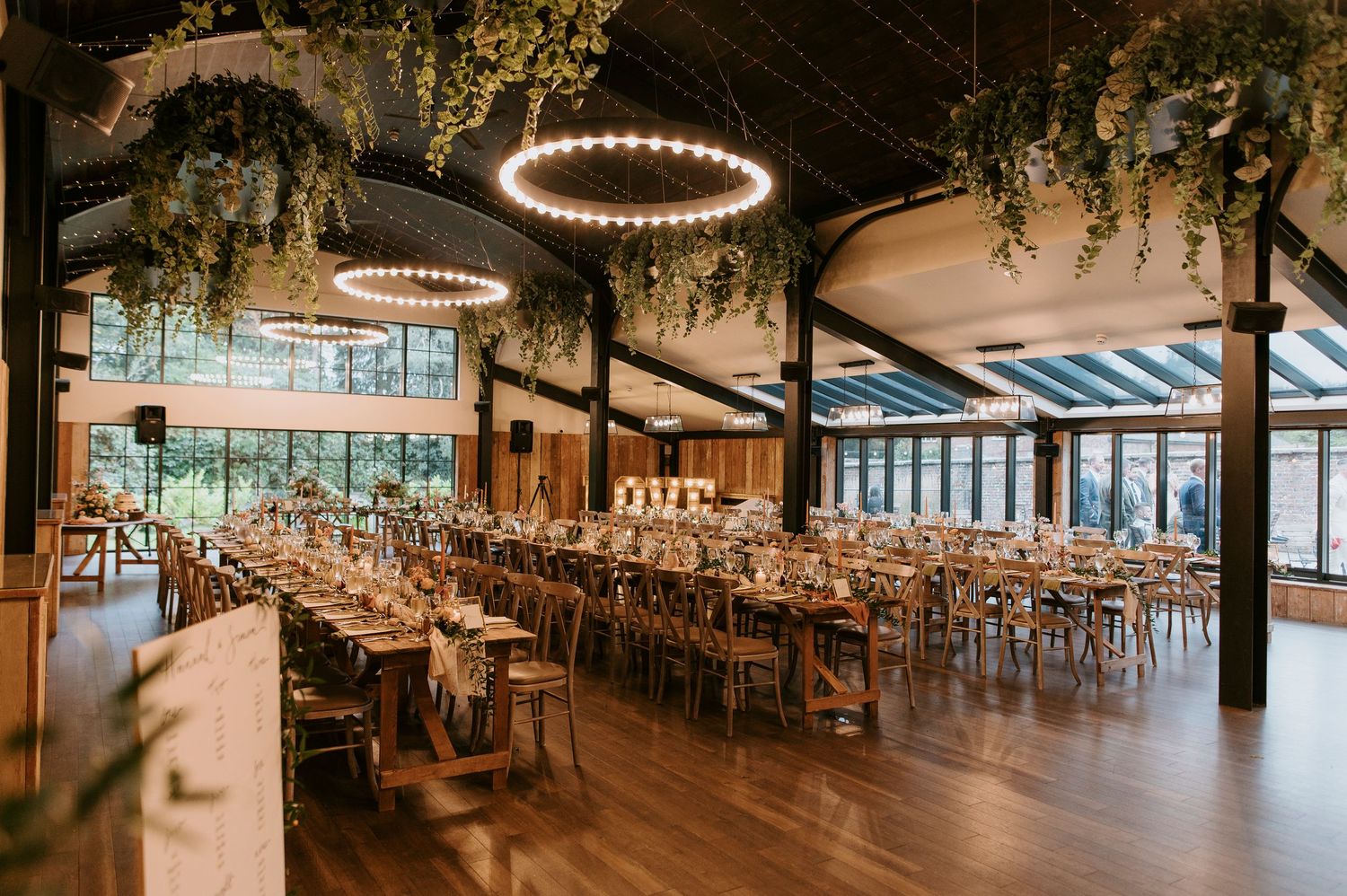 Elegant wedding reception venue with circular chandeliers, rustic wooden beams, and natural light streaming through windows.