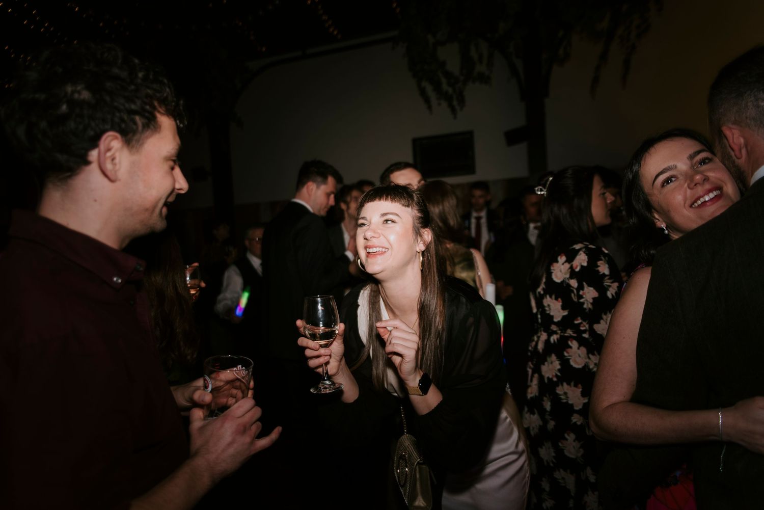 People enjoying drinks and conversation at a dimly lit social gathering or party.