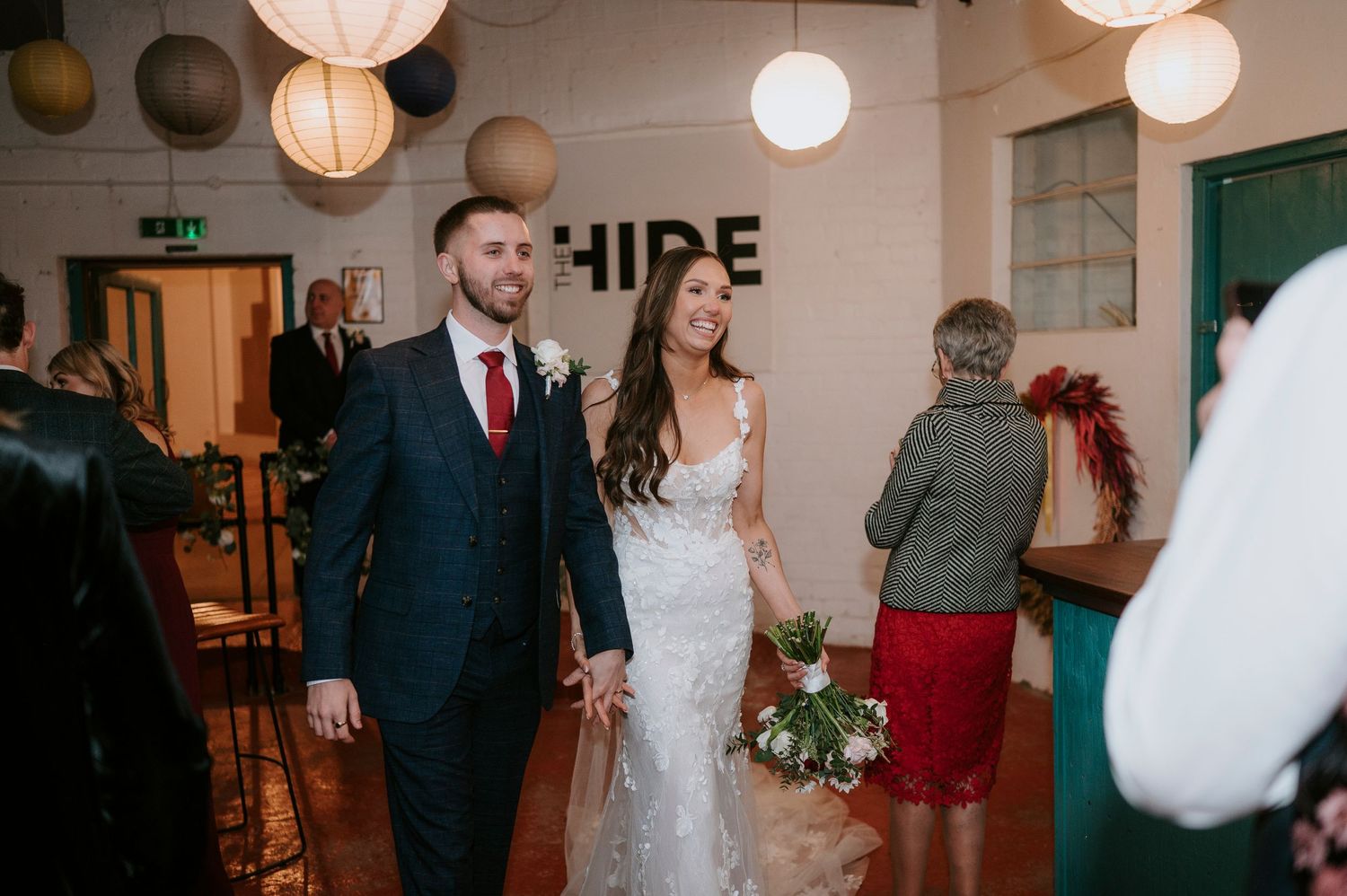 Happy newlyweds walk hand-in-hand through wedding venue adorned with round paper lanterns.