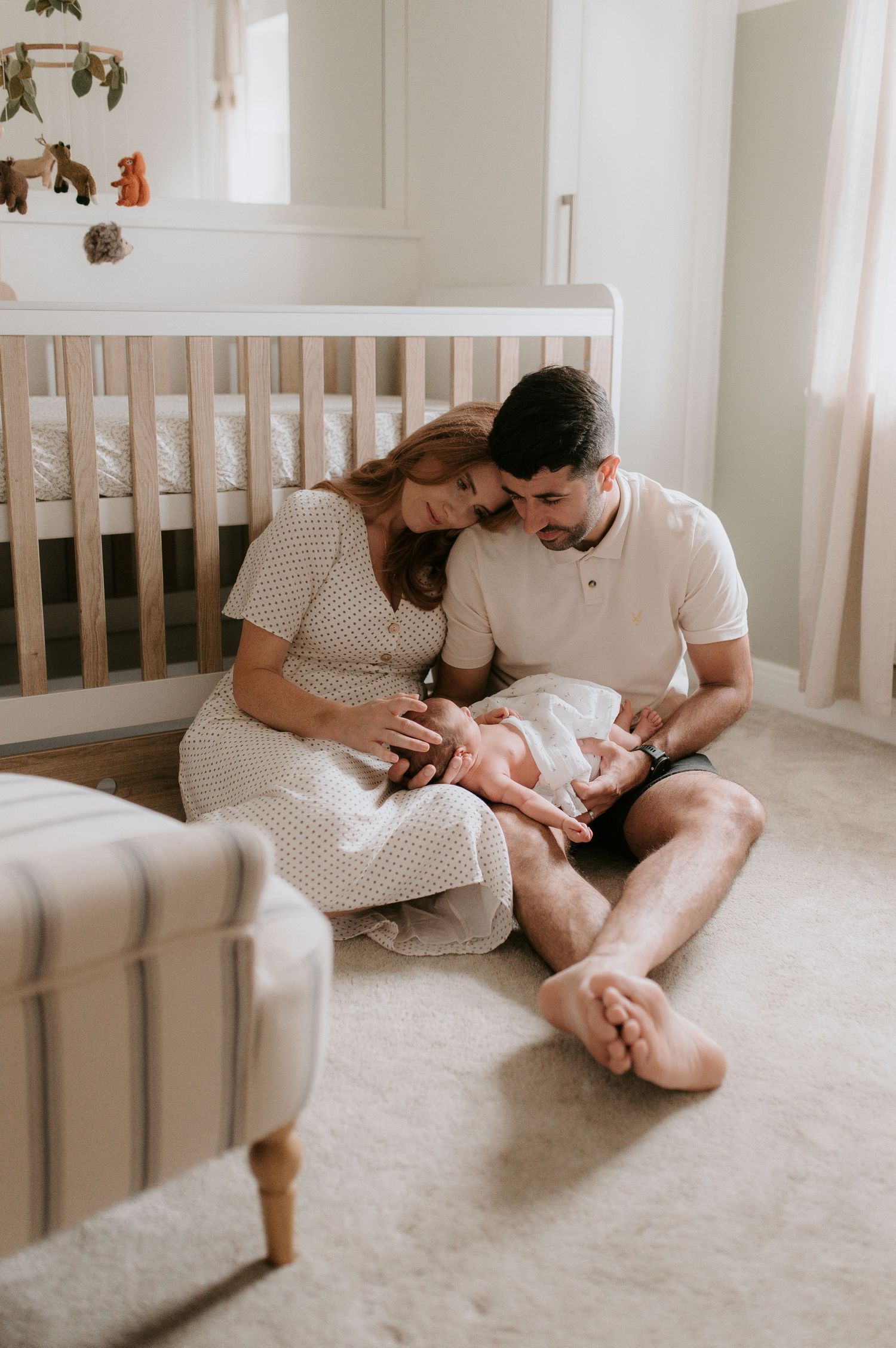 Parents lying on floor with baby in bright white nursery room with crib and carpet.