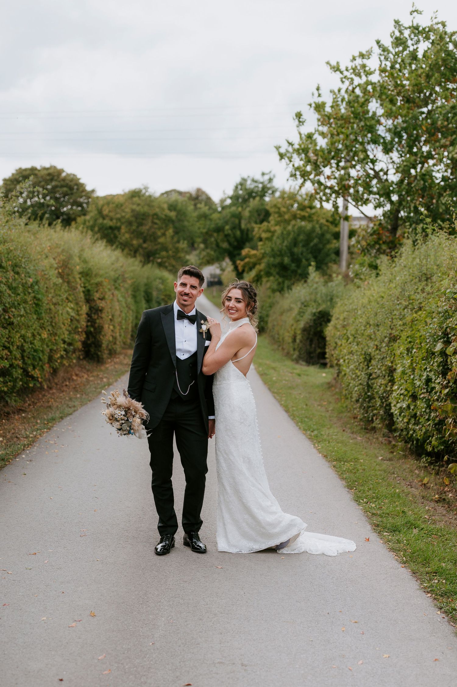 A bride and groom walk hand in hand down a tree-lined path on their wedding day.