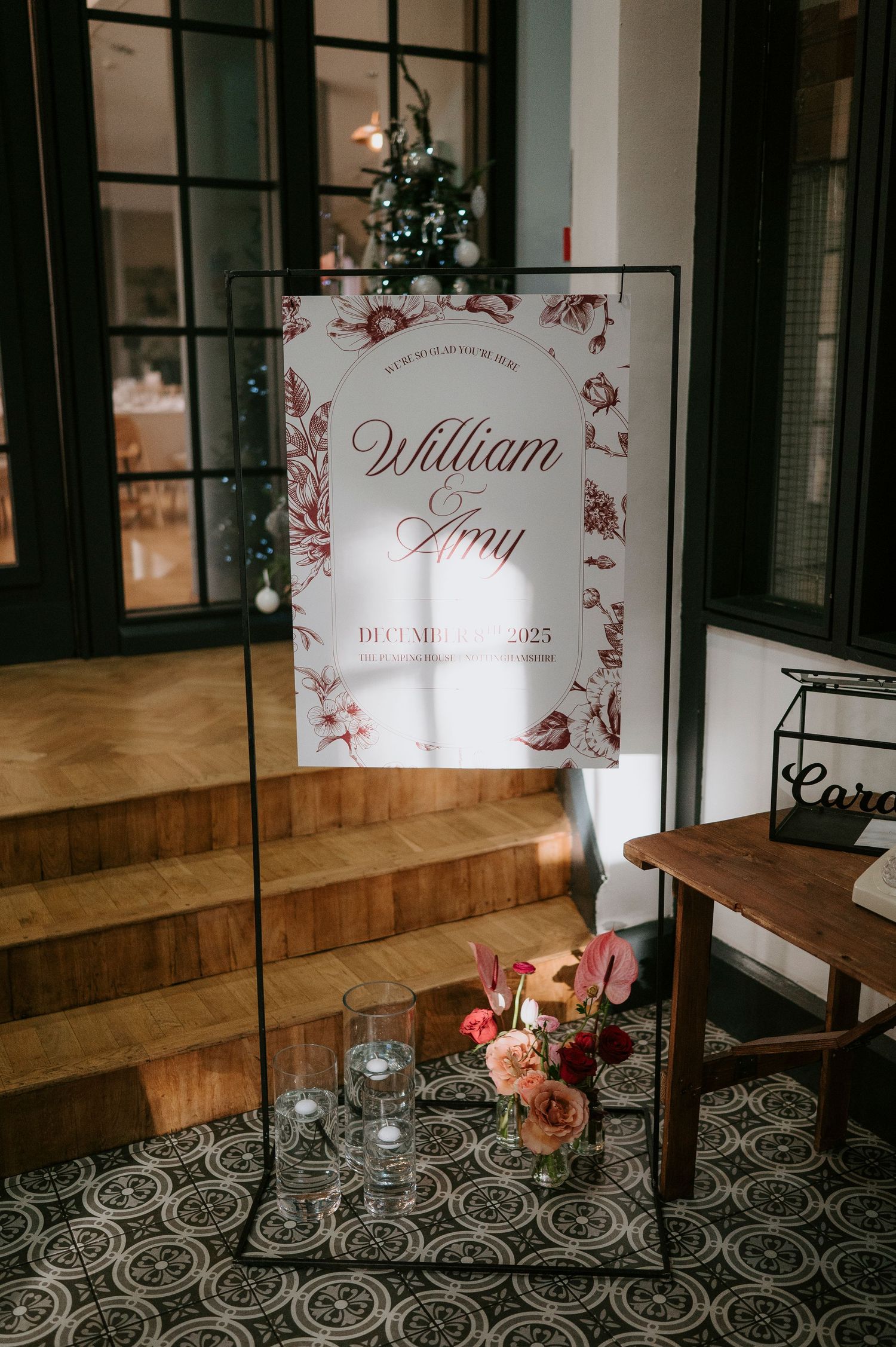 Elegant wedding seating signs with floral designs displayed on wooden steps with decorative lighting and flowers.