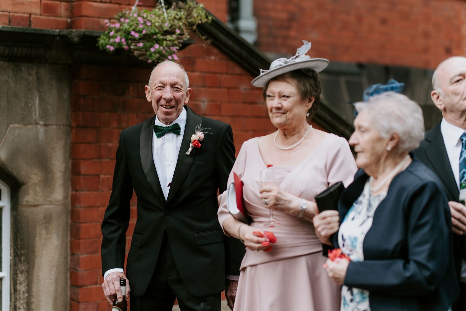 Wedding guests throw confetti and celebrate outside a red brick building during a joyous celebration.