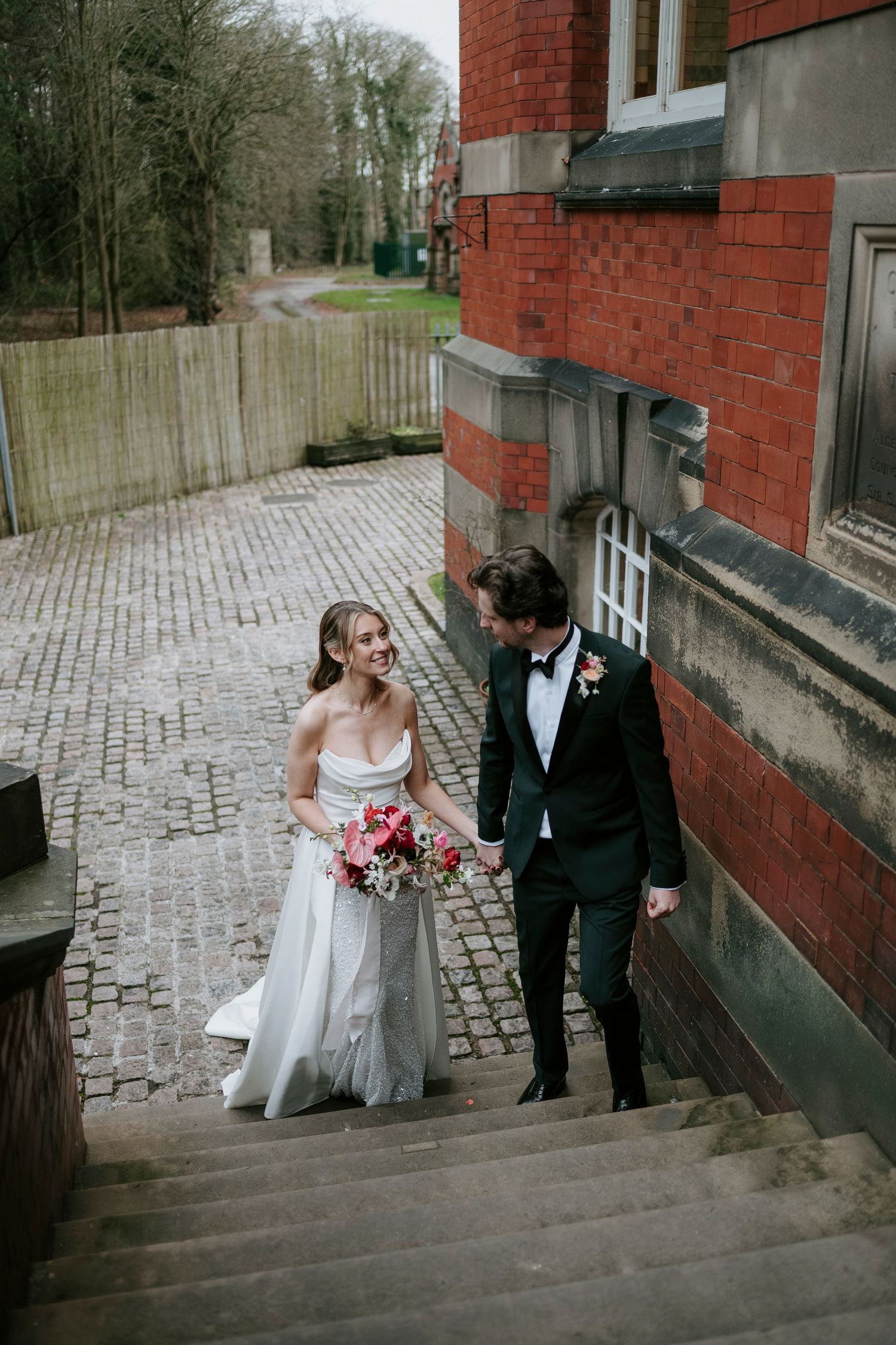 A romantic wedding couple shares a tender moment on cobblestone steps outside a brick building.