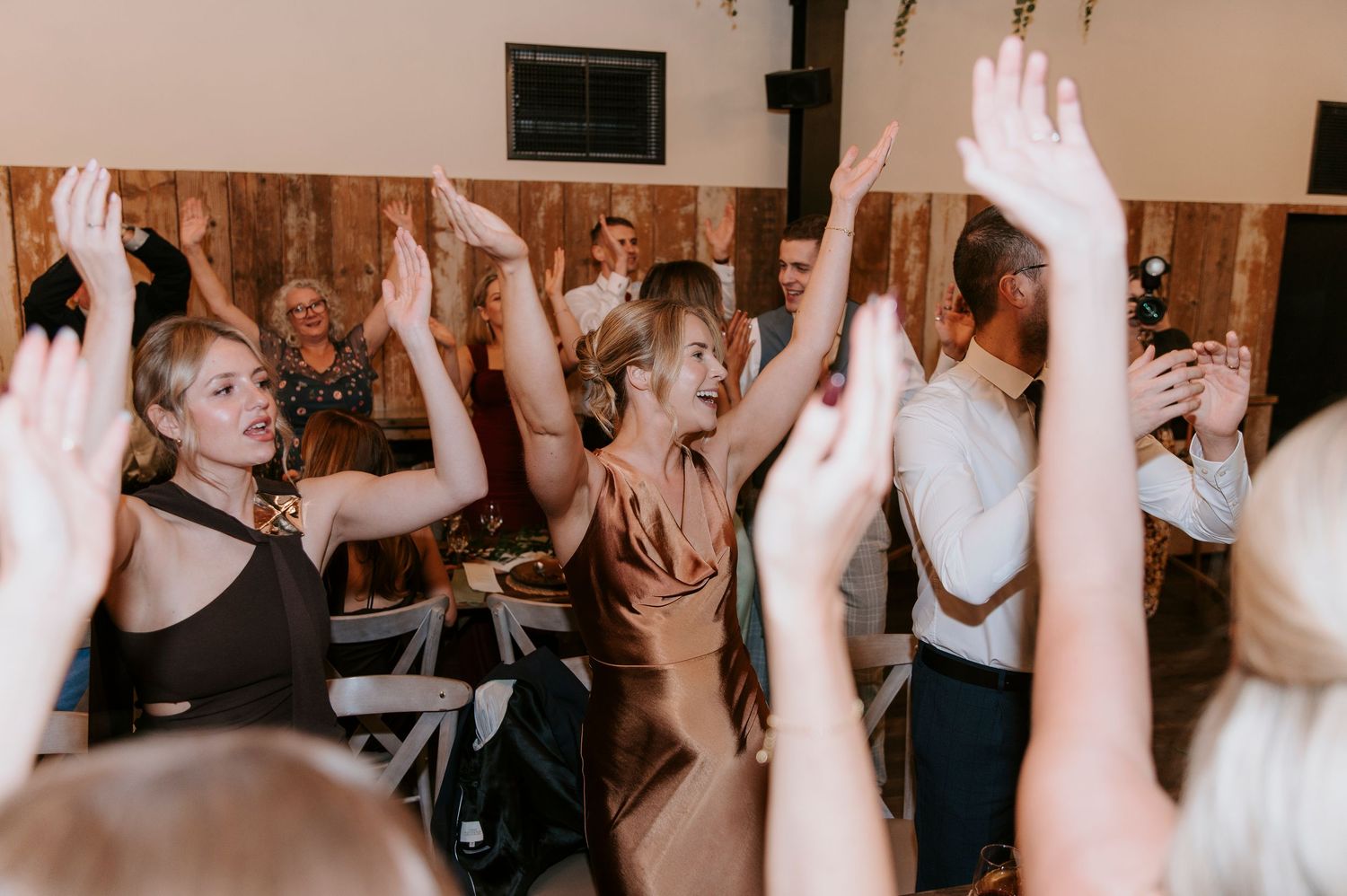 A crowd of people dancing with their hands raised in a dimly lit room during a celebration or party.