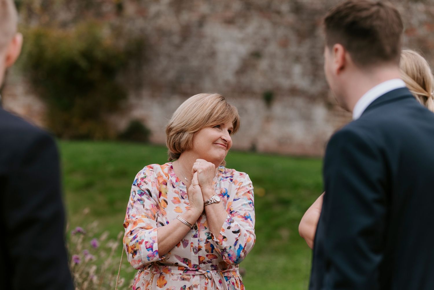 A guest in a floral dress reacts emotionally during an outdoor wedding ceremony.