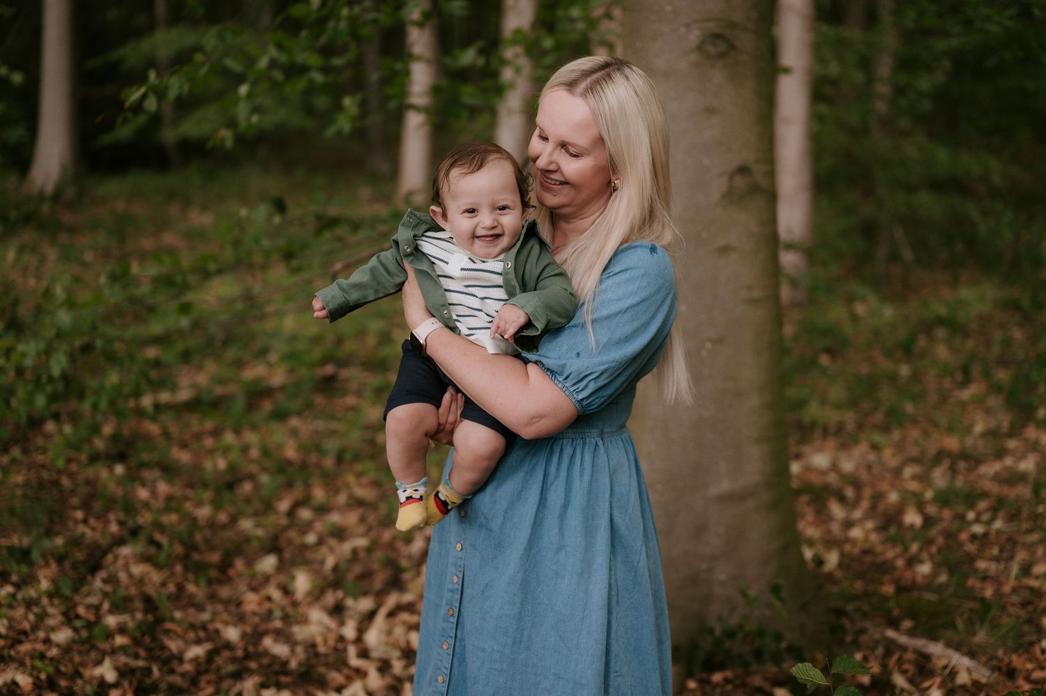 A parent and child share a tender moment while walking through a wooded area with fallen autumn leaves.