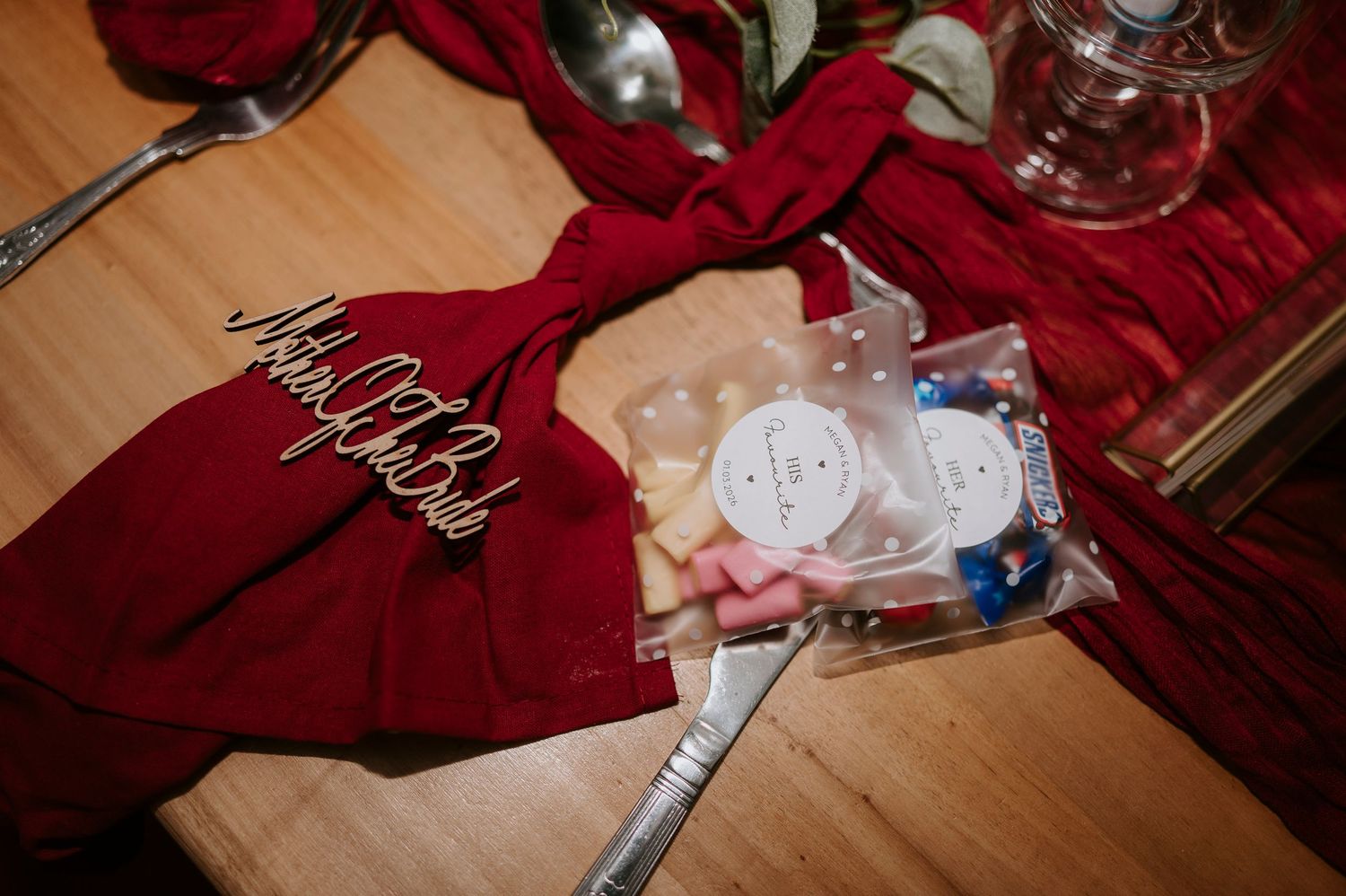Red satin robe with gold script lettering beside a wedding emergency kit bag on a decorated table.