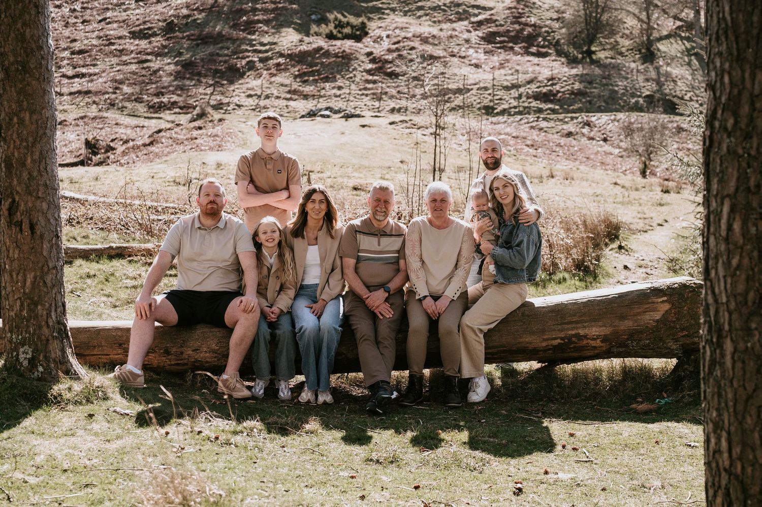 A group of people sitting together on a fallen log in a rustic outdoor setting.