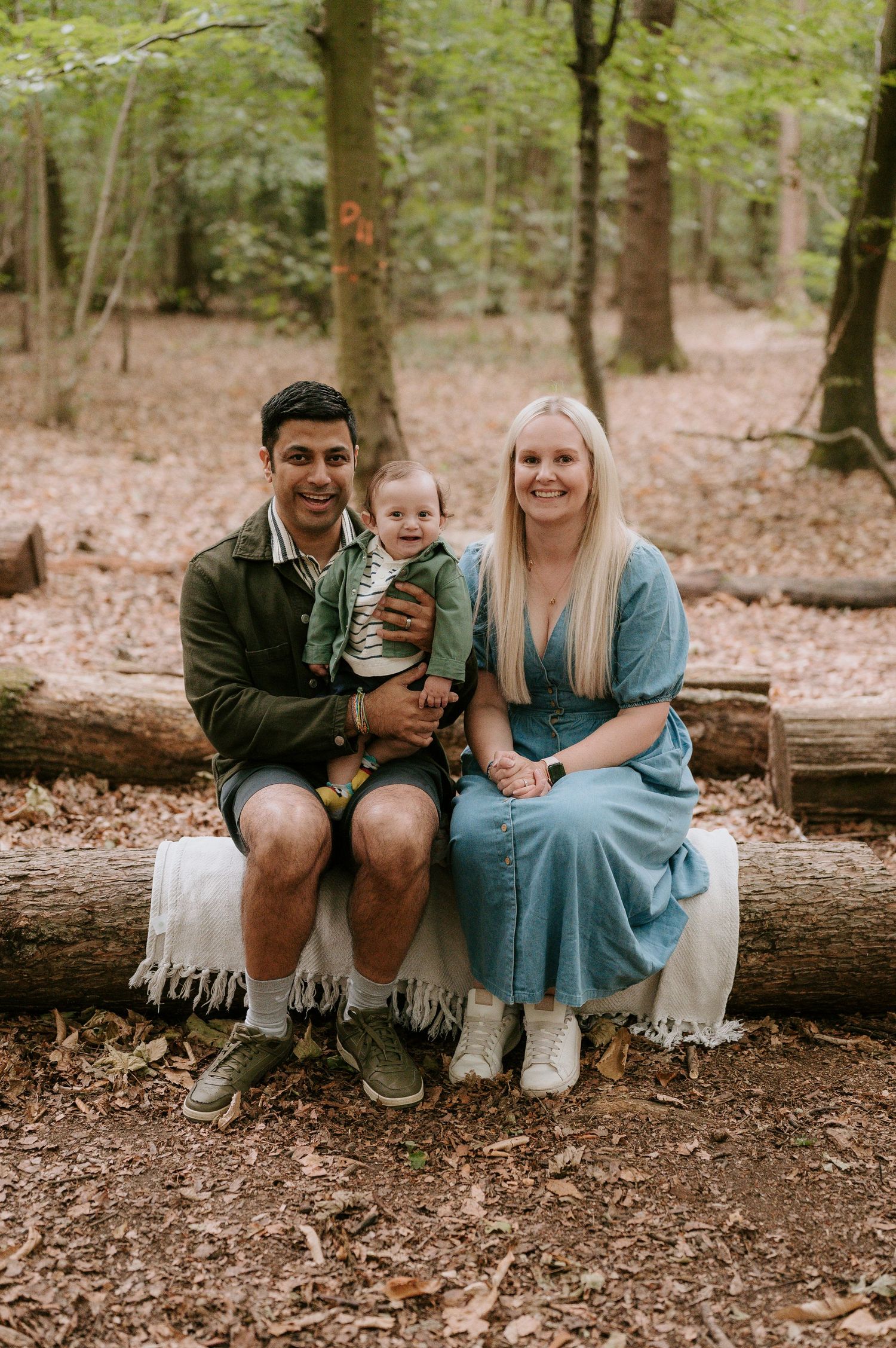 A family sits together on a fallen log in a wooded area during an outdoor photo session.