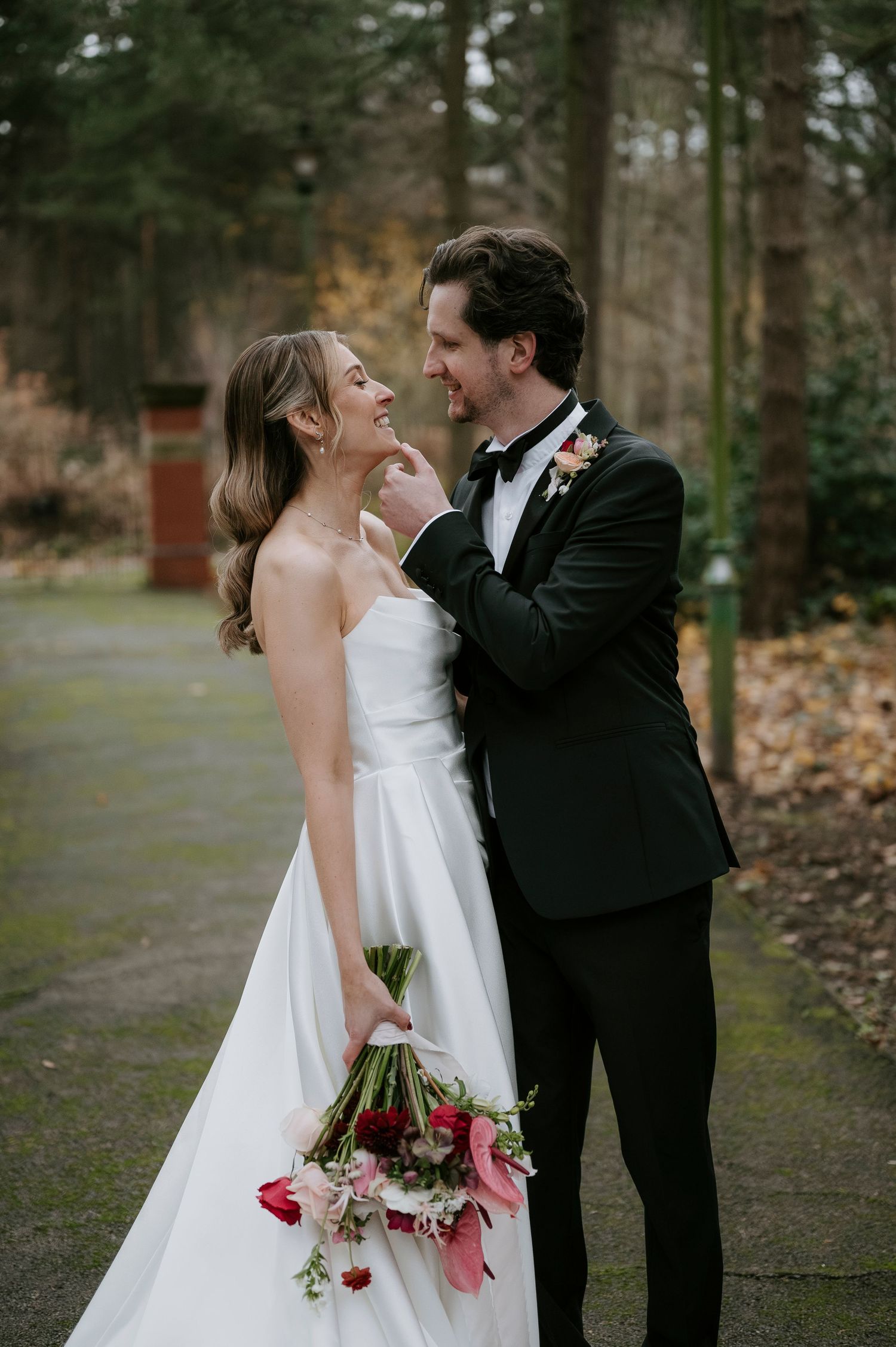 Romantic wedding couple shares intimate moments in a wooded outdoor setting with fall foliage and red flowers.