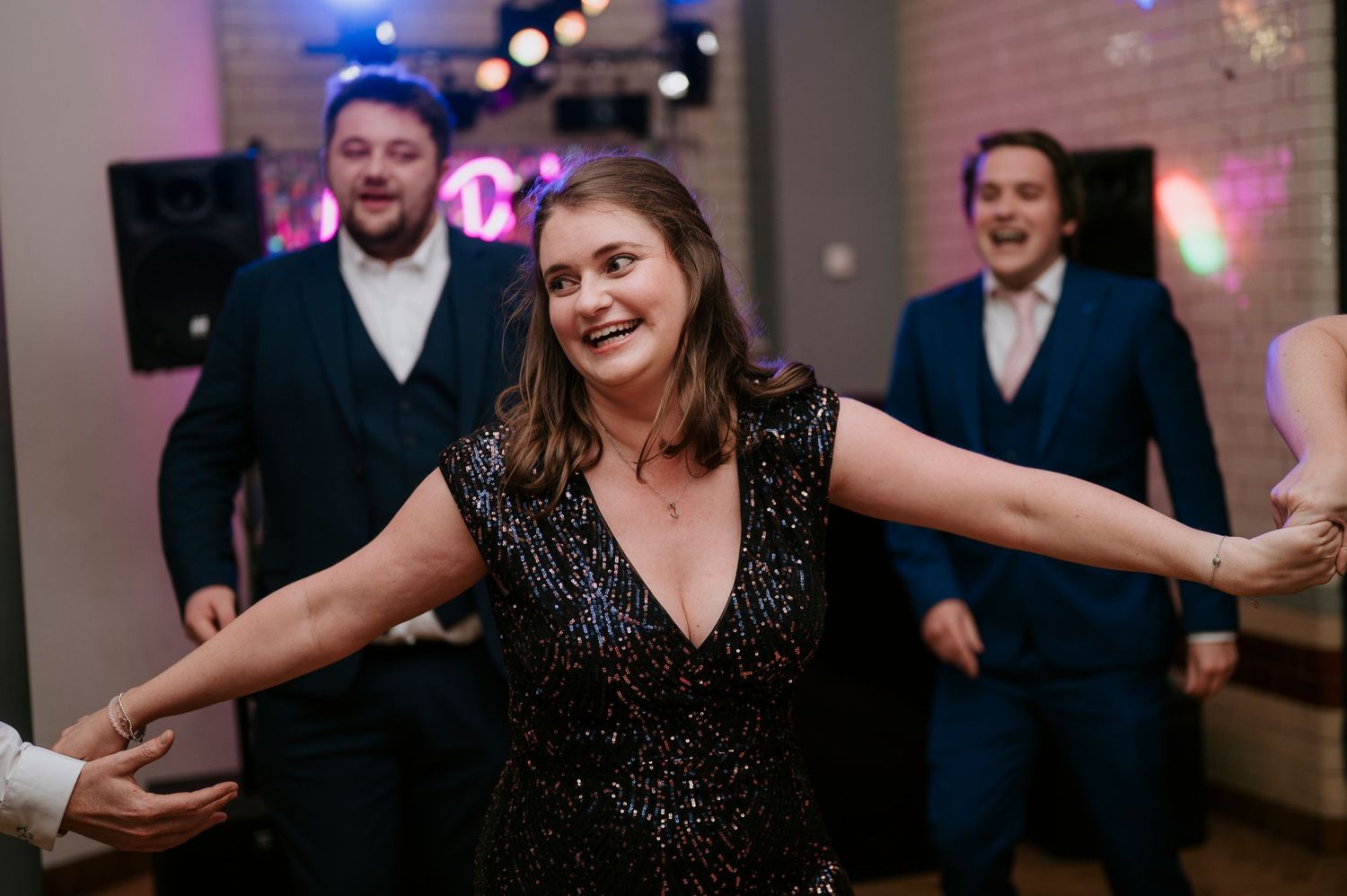 Wedding reception guests dance and celebrate under colorful party lights indoors.