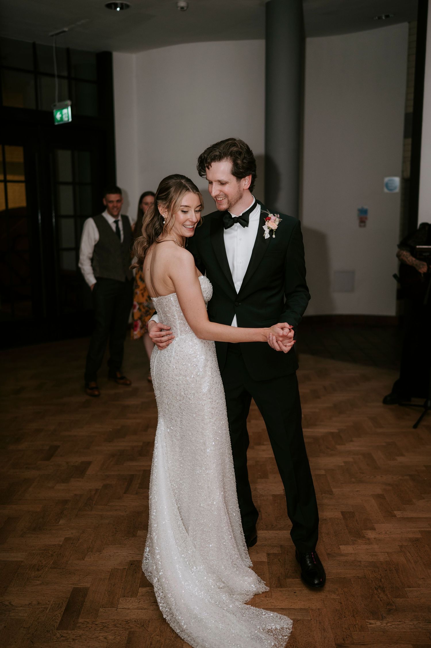 A couple shares an intimate dance moment on a wooden floor during their wedding reception.