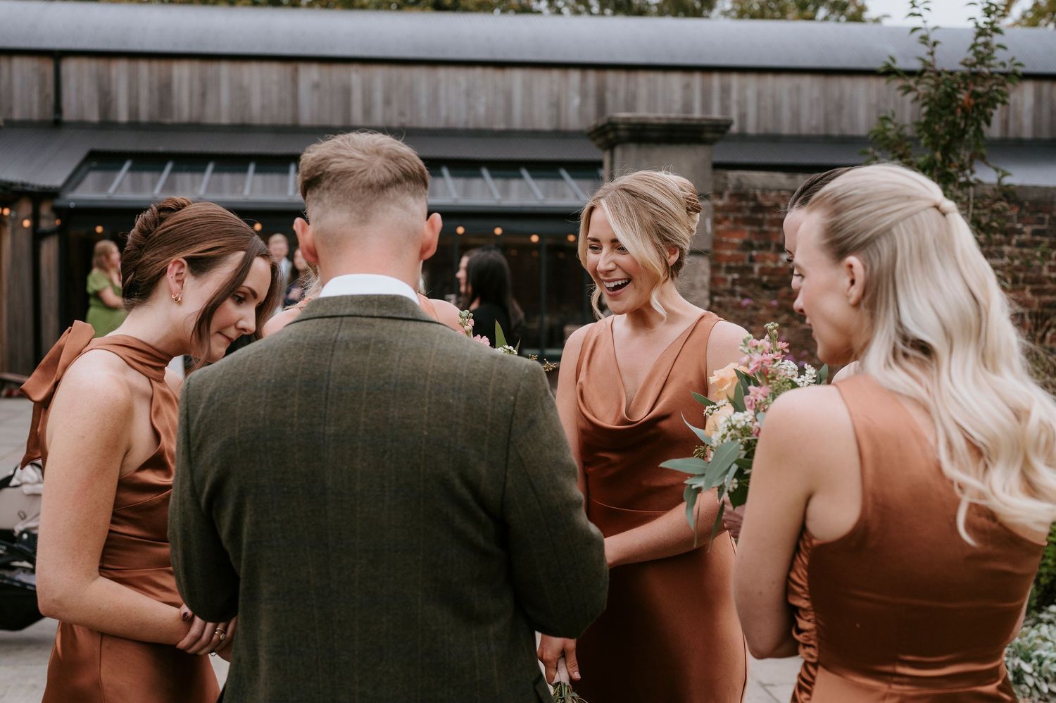 Wedding party laughs and embraces during an outdoor celebration in warm afternoon light.