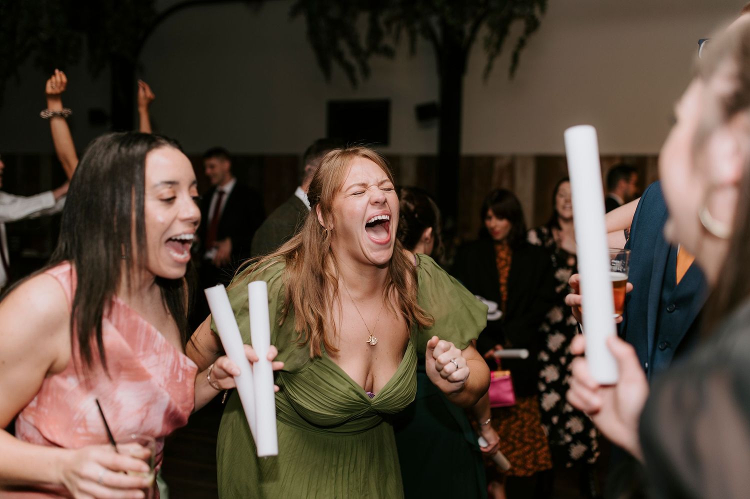 Wedding guests dance and laugh while holding glow sticks during an energetic reception celebration.
