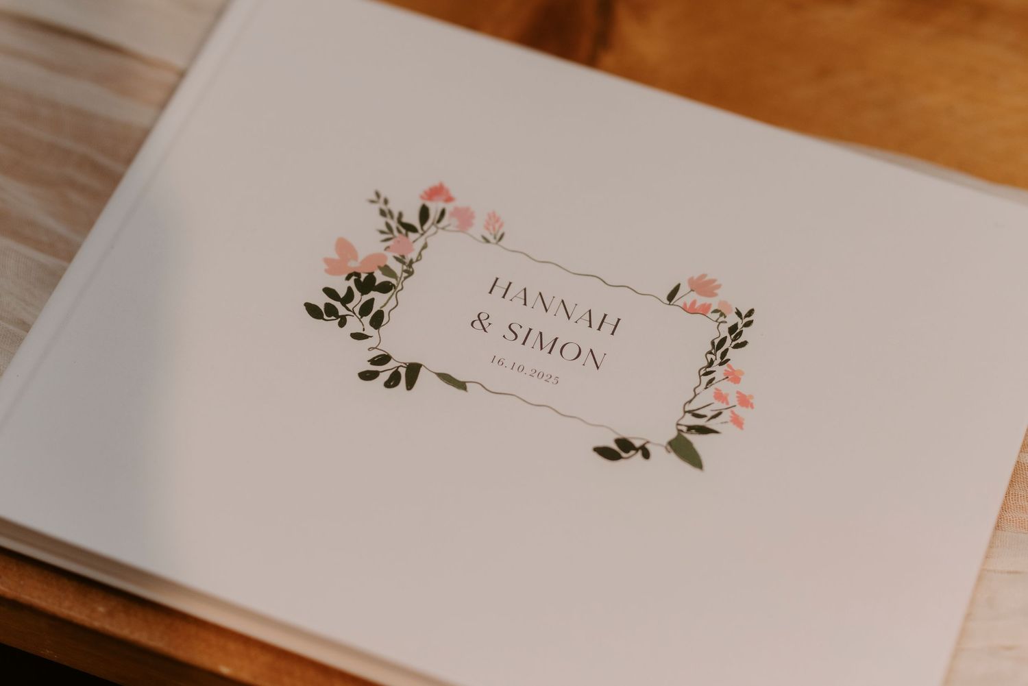 Wedding invitation with floral design and elegant calligraphy sits on a wooden surface.