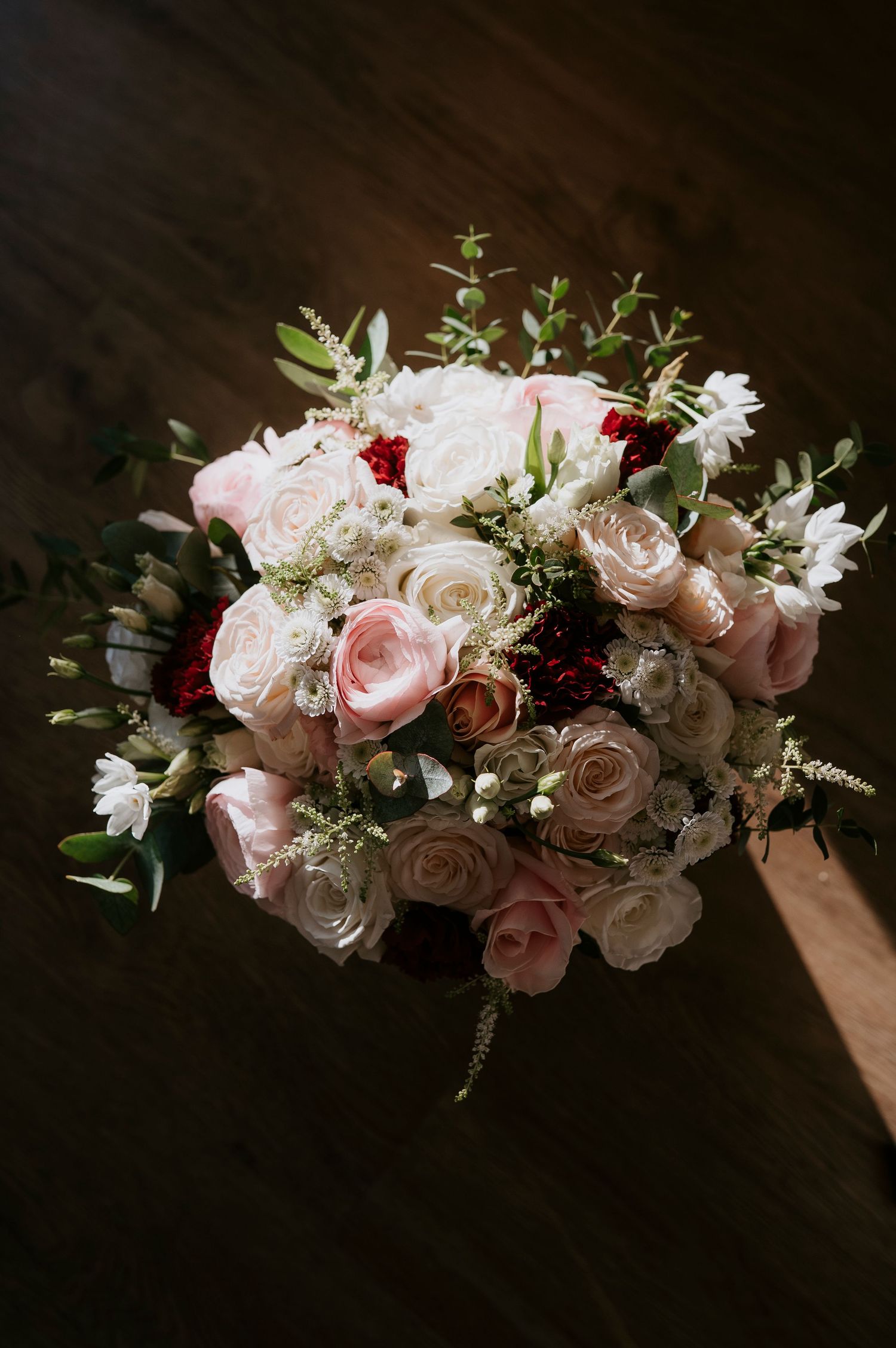 Elegant bridal bouquet with pink, white, and red roses accented by eucalyptus greenery on a dark wood surface.