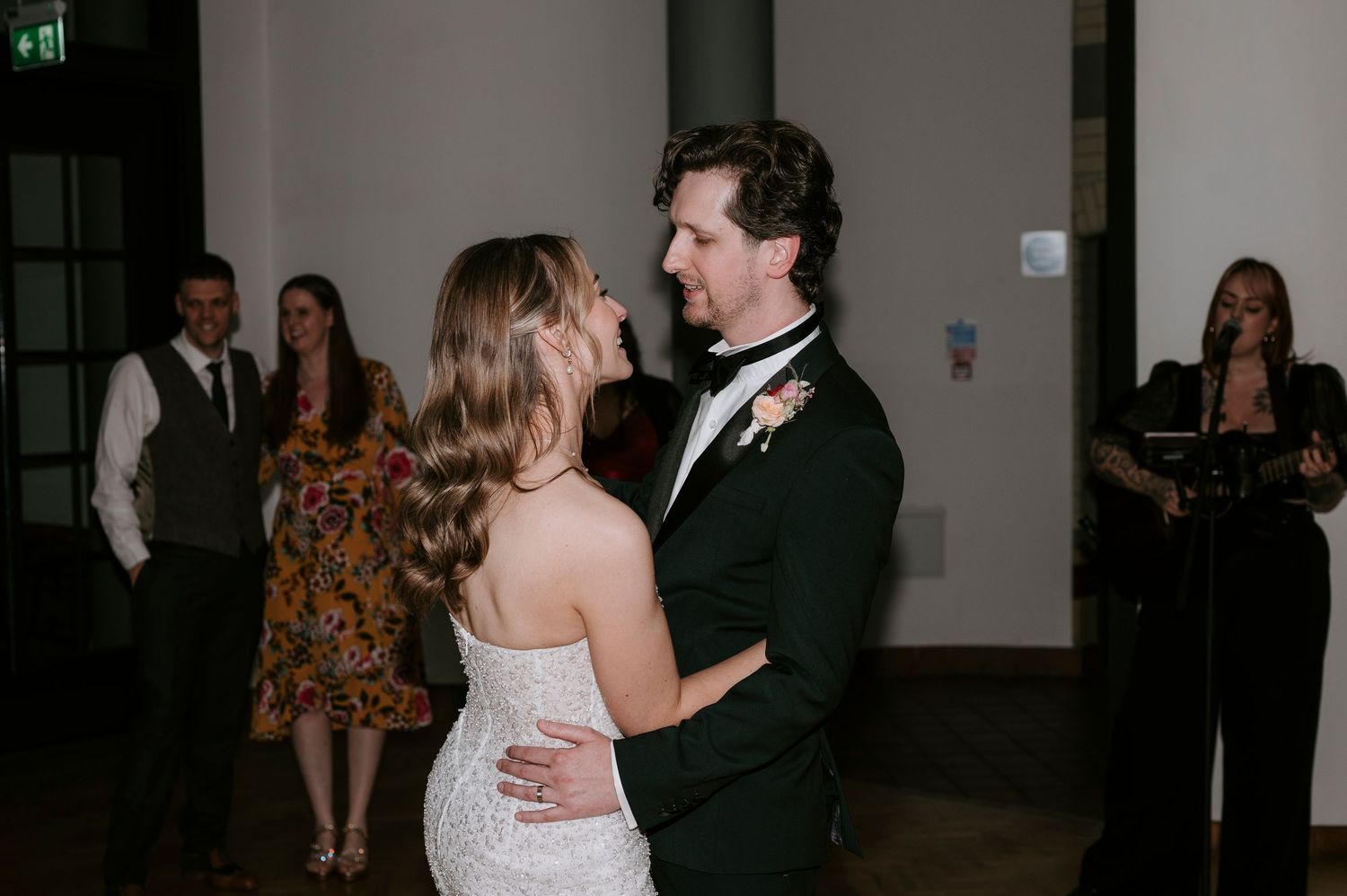 Wedding guests dance and celebrate on a wooden dance floor at an indoor reception venue.