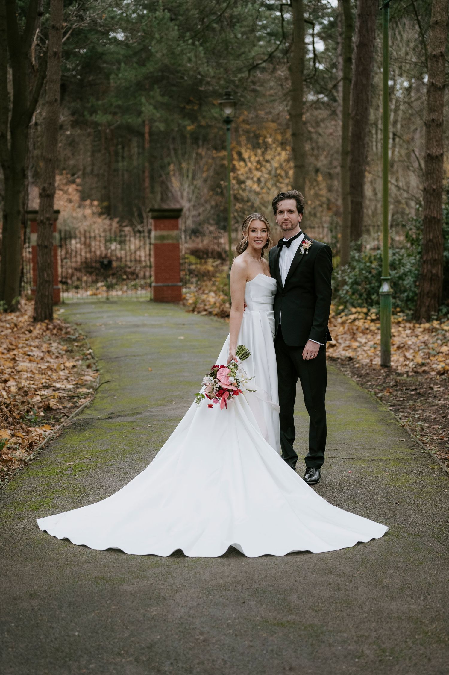 Elegant wedding photos taken on a wooded path with fallen autumn leaves.