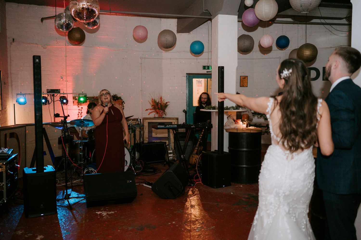 Bride watches live band perform at wedding reception venue decorated with colorful balloons.