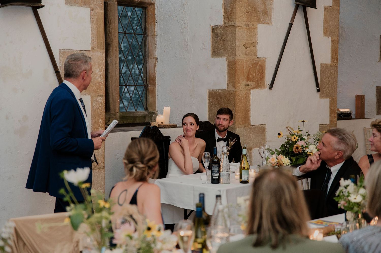 Wedding reception dinner setup in an elegant stone-walled venue with floral centerpieces.