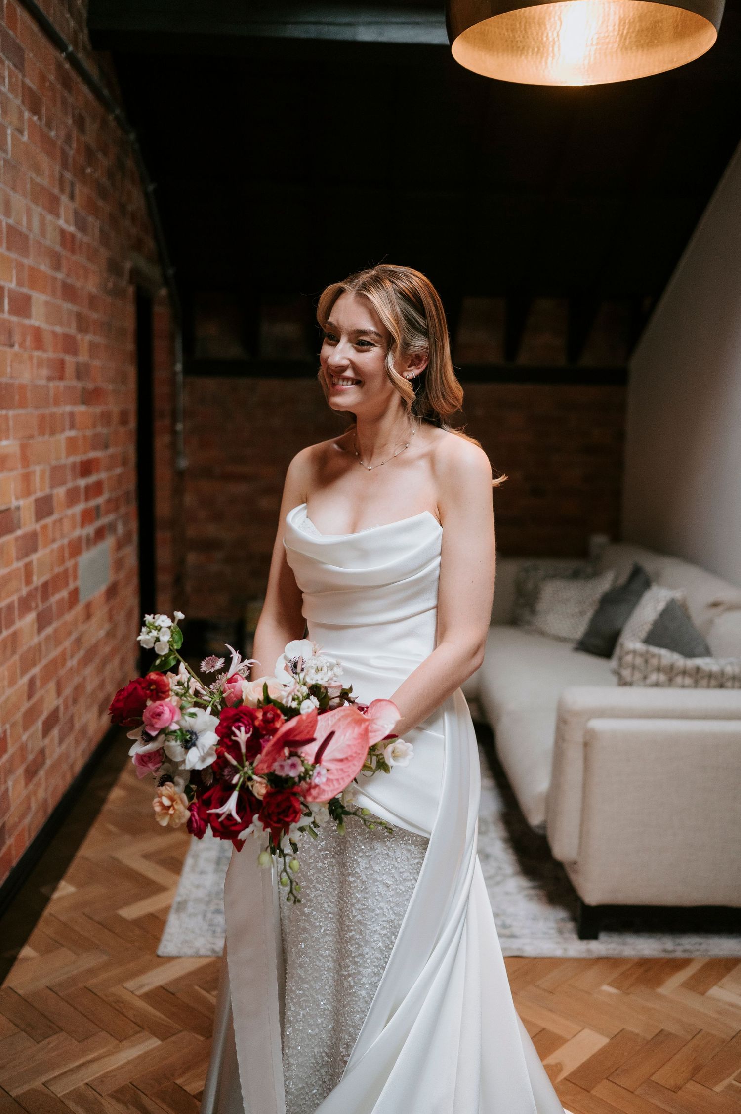 A bride holds a vibrant burgundy and pink wedding bouquet against her white gown in an industrial-style venue.