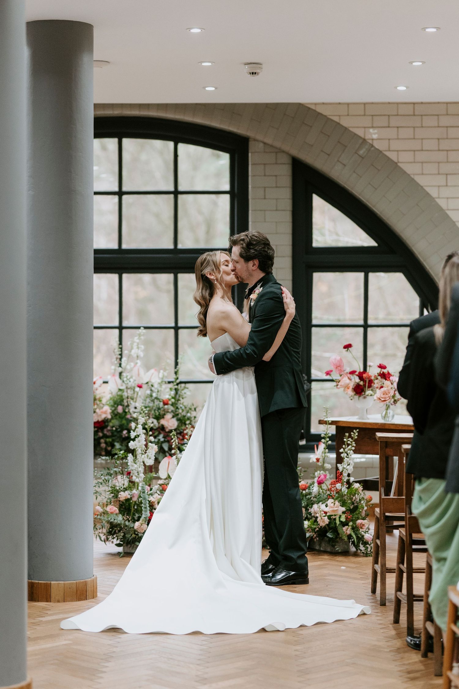 Wedding couple shares their first dance in an elegant venue with arched windows and floral decorations.