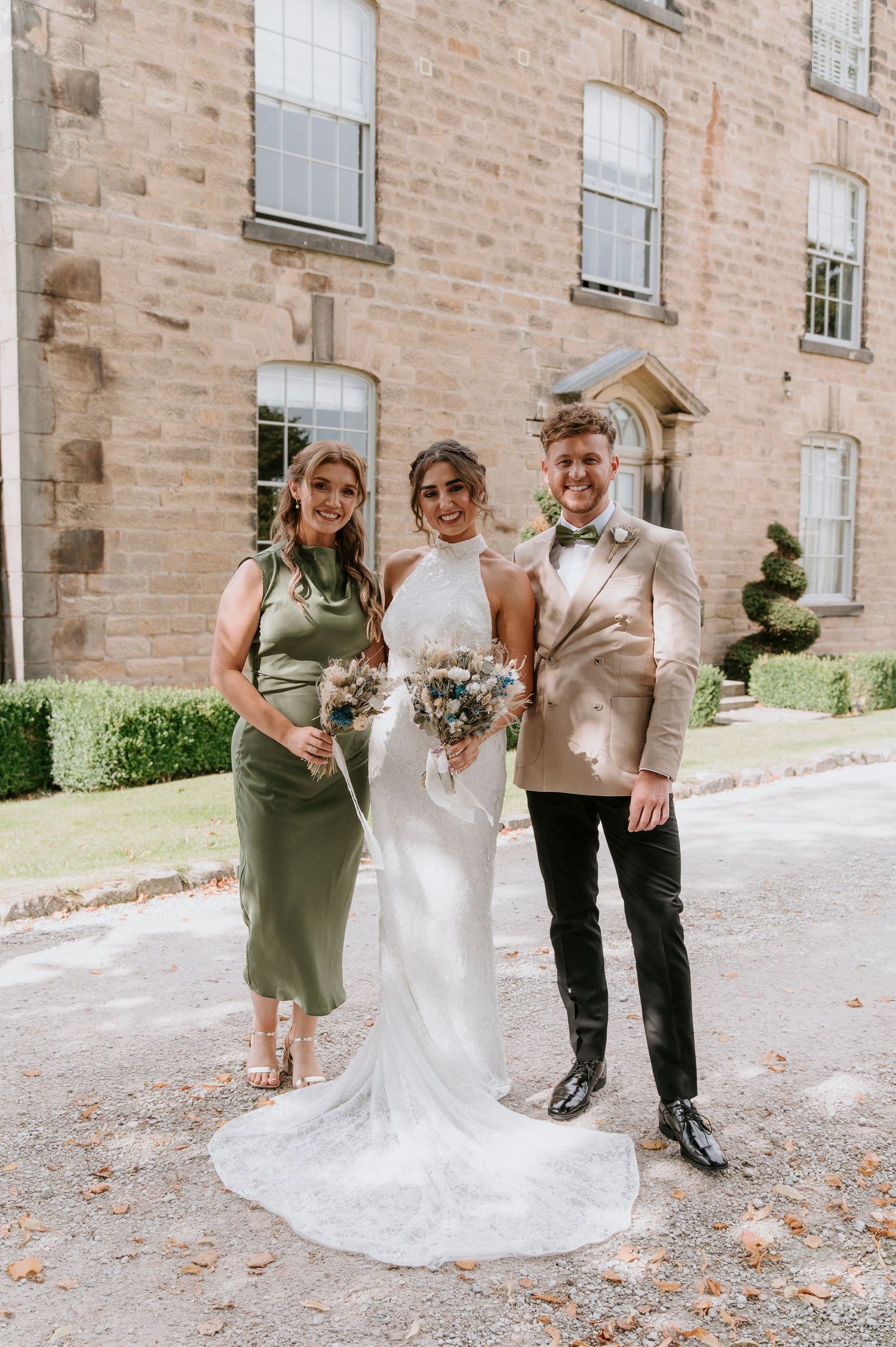 Wedding party poses together outside historic brick building with sage green bridesmaid dresses and white bridal gown.