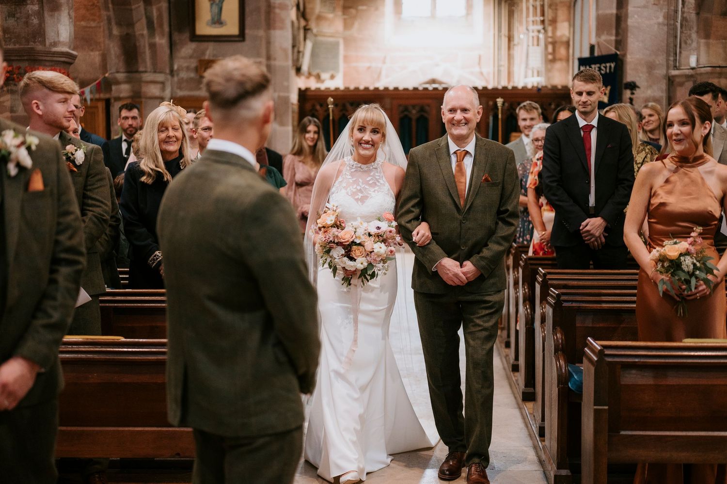 A traditional church wedding ceremony with the bride walking down the aisle accompanied by a gentleman in a suit.