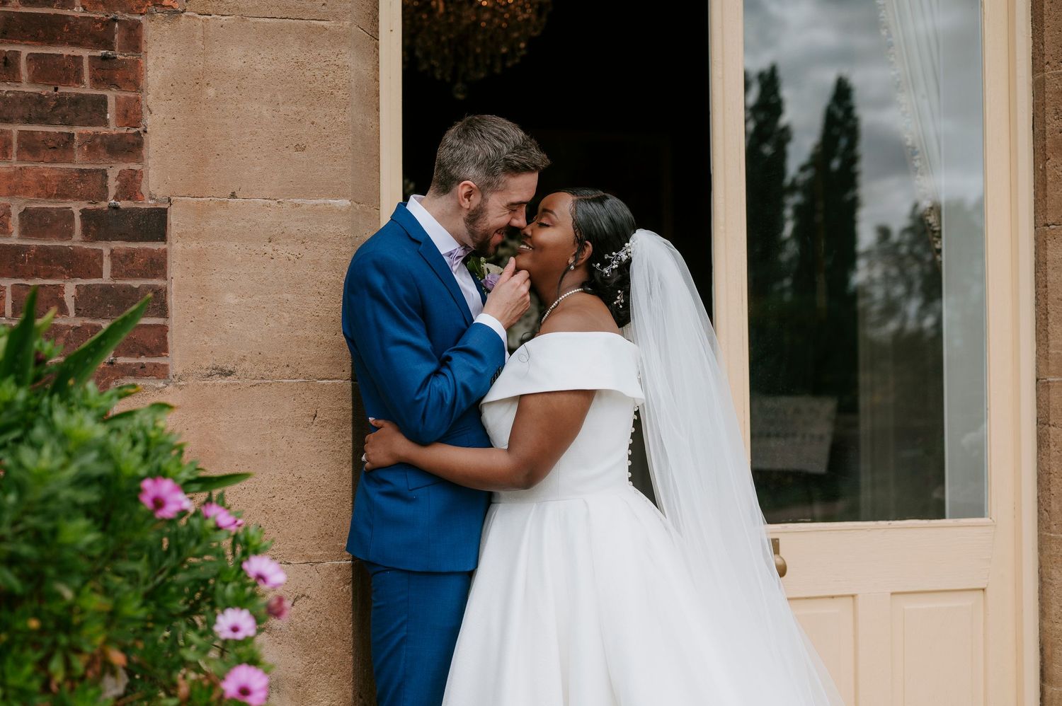 A couple in wedding attire share an intimate moment against a brick wall backdrop during their wedding celebration.