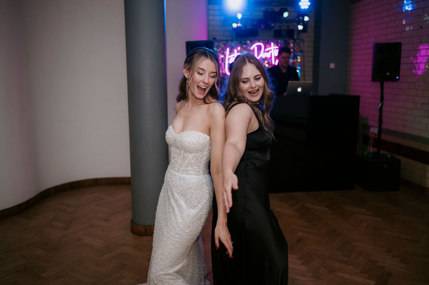 Wedding party dancing under pink and blue mood lighting at indoor reception.