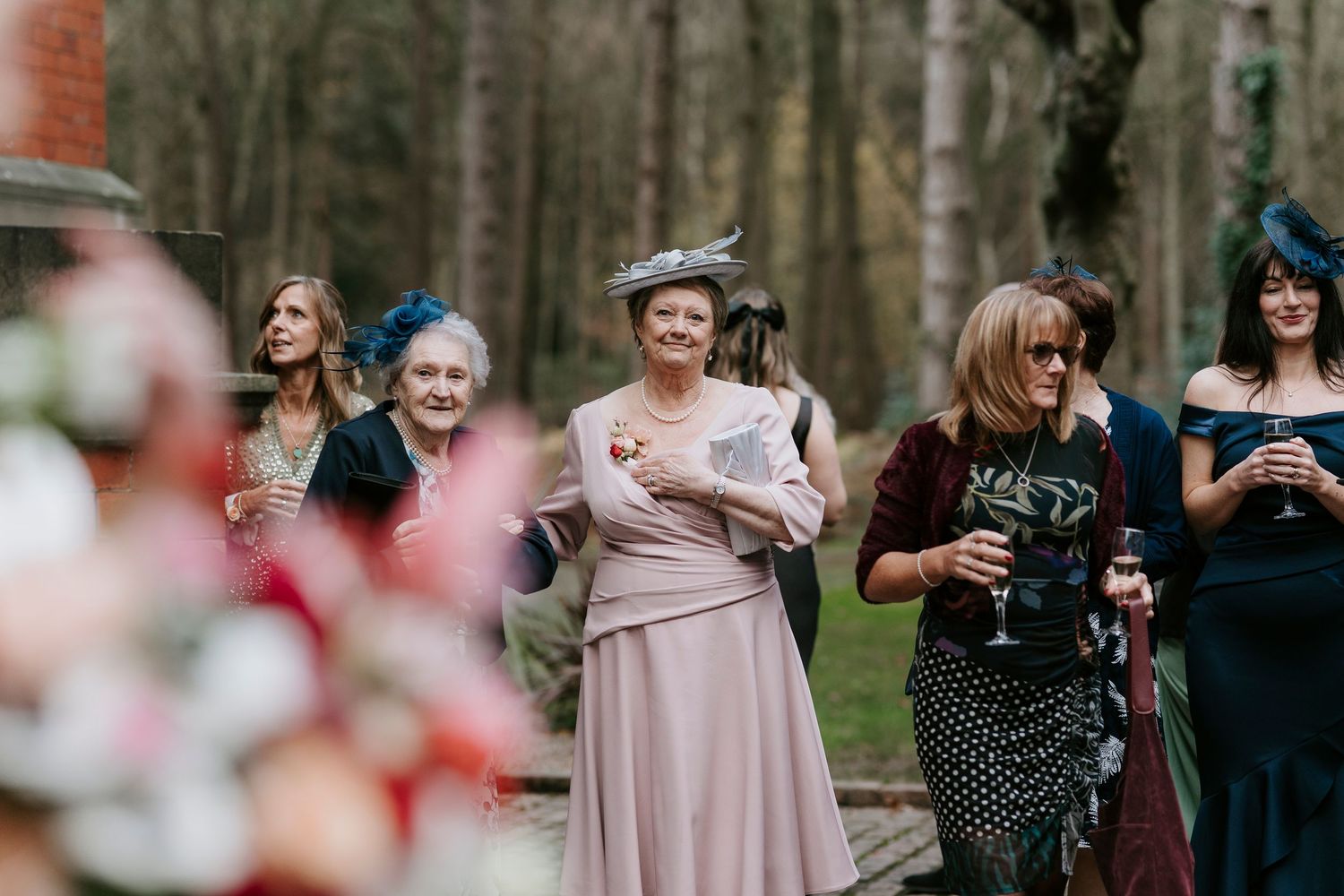 Wedding party in pink and dark dresses poses together outdoors among trees.