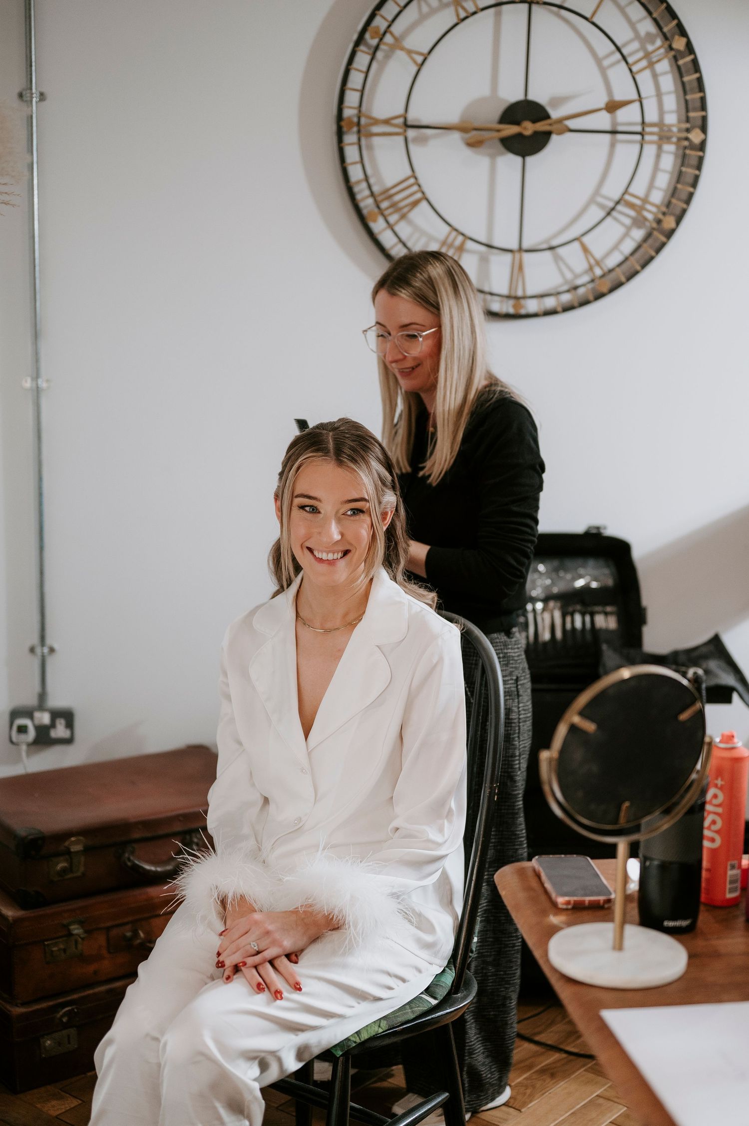 Bride in white suit getting hair styled beneath large vintage clock.