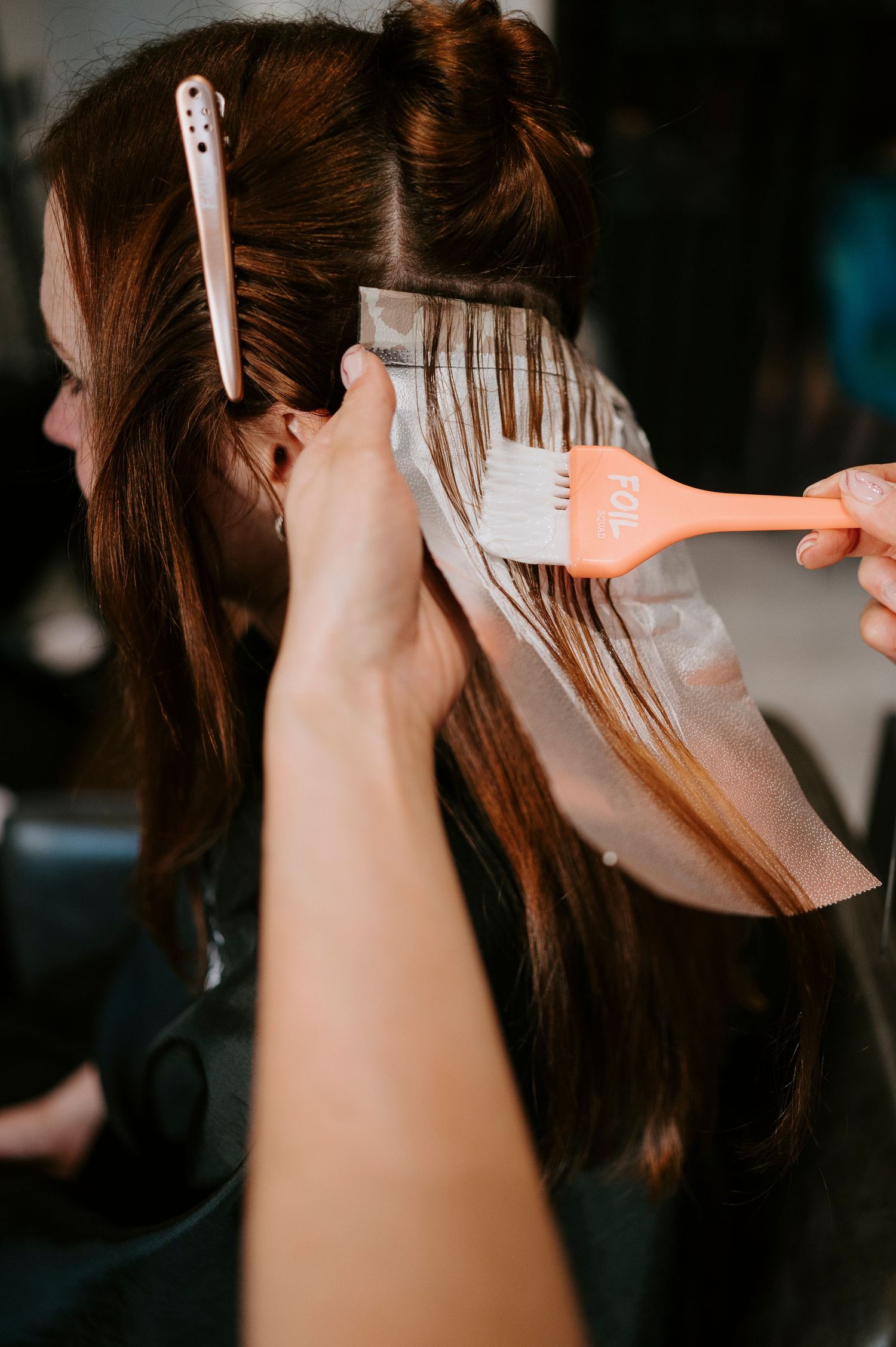 A hairstylist uses a comb to section brown hair during a professional styling session at a salon.