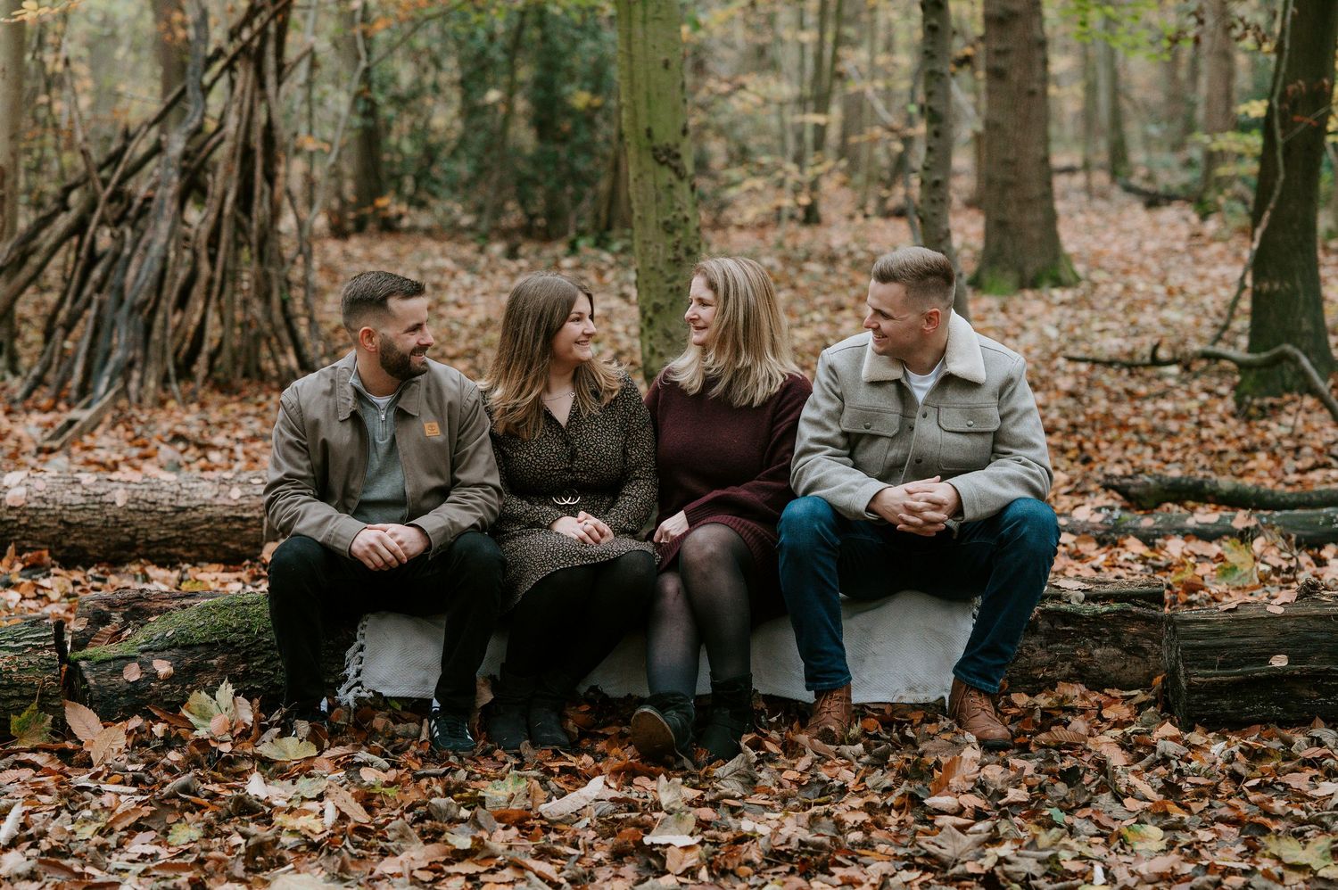 Four friends sitting on fallen logs in an autumn forest covered with brown leaves.