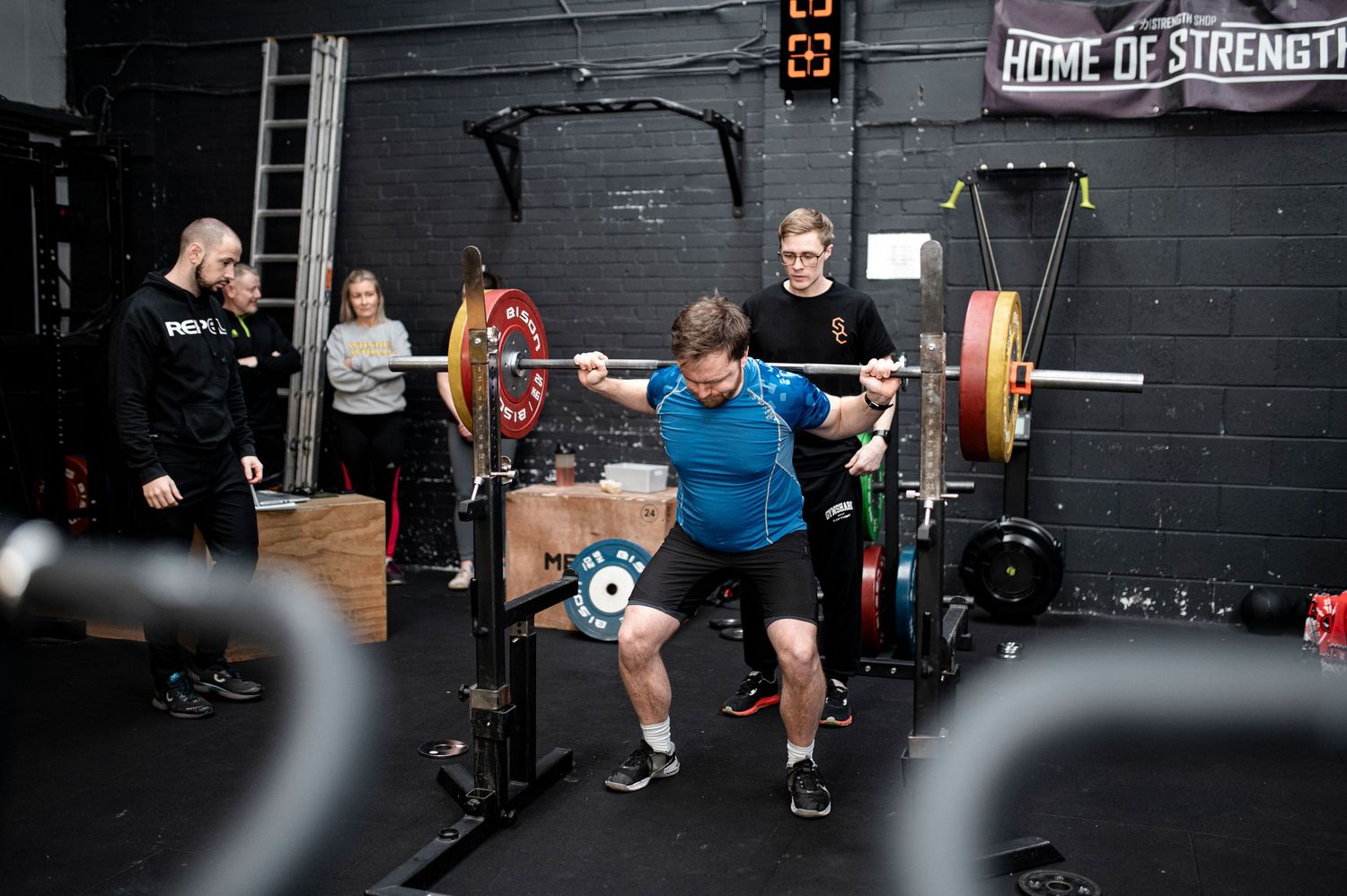Athletes perform various exercises at a CrossFit-style gym with black walls and fitness equipment.