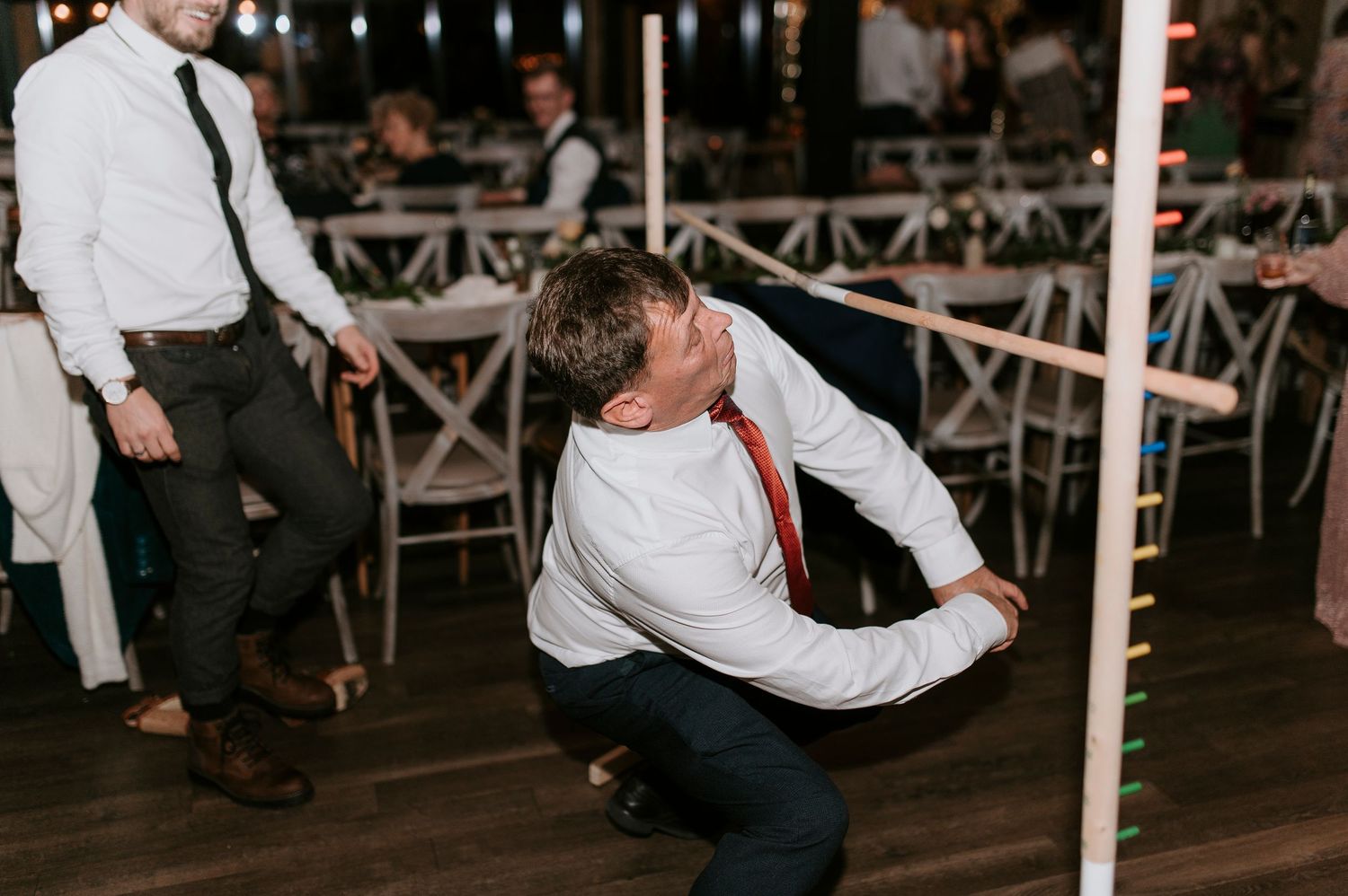 People dancing and celebrating at a wedding reception with white chairs and rustic decor visible in the background.